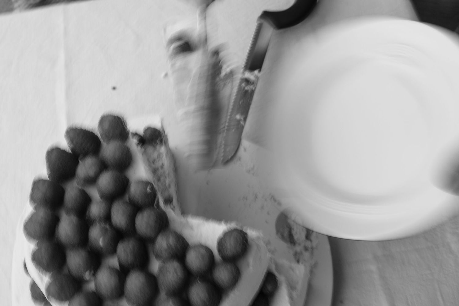 Black and white overhead shot of hands cutting a cake decorated with round chocolate truffles.