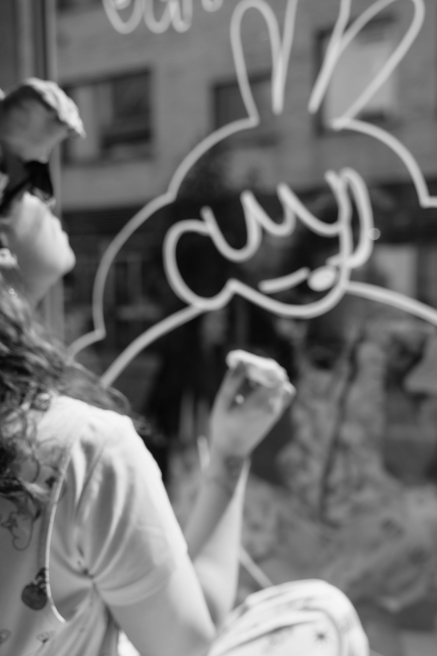 Black and white photo of woman drawing a cartoon bunny outline on a glass storefront window.