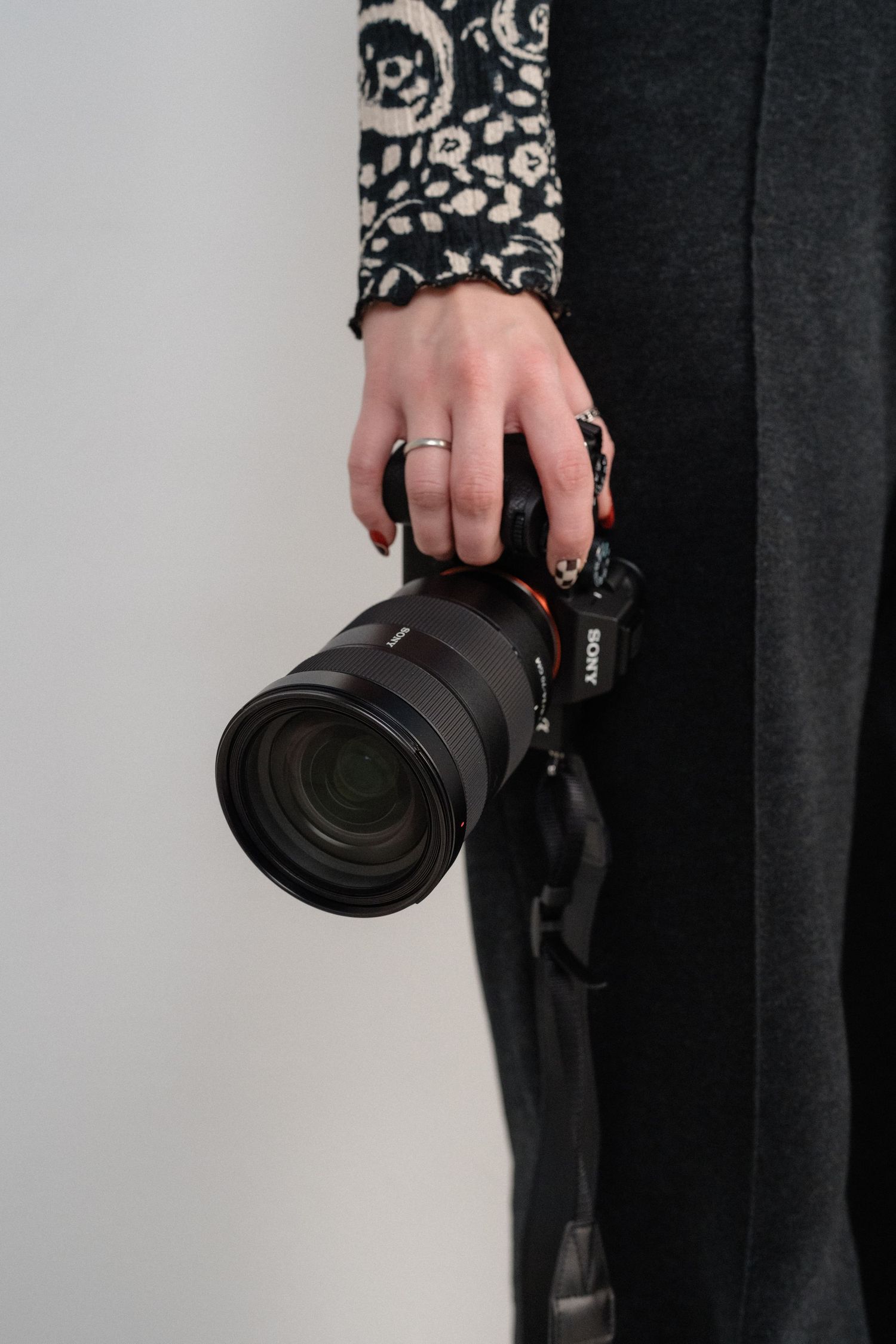 Photographer holding a professional Sony camera with zoom lens while wearing casual black and patterned clothing.
