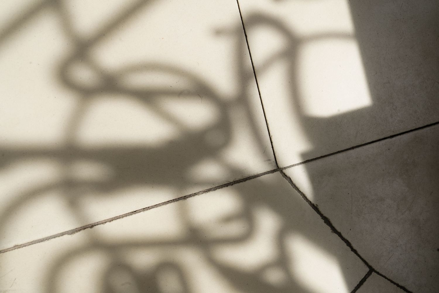 Abstract shadow of neon sign tubes cast on light beige floor tiles.