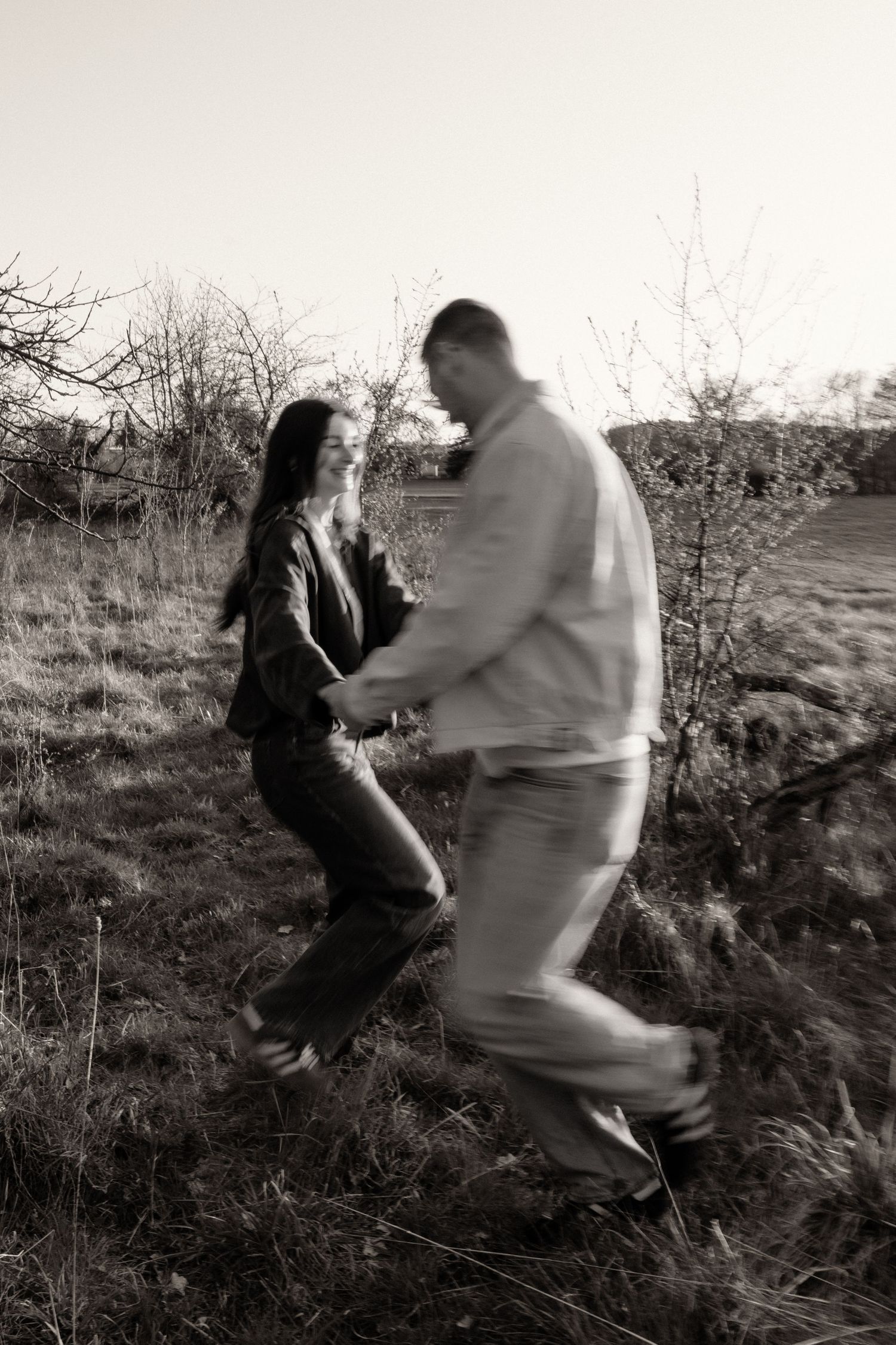 Black and white motion-blur photo of couple running and holding hands in a rural landscape.