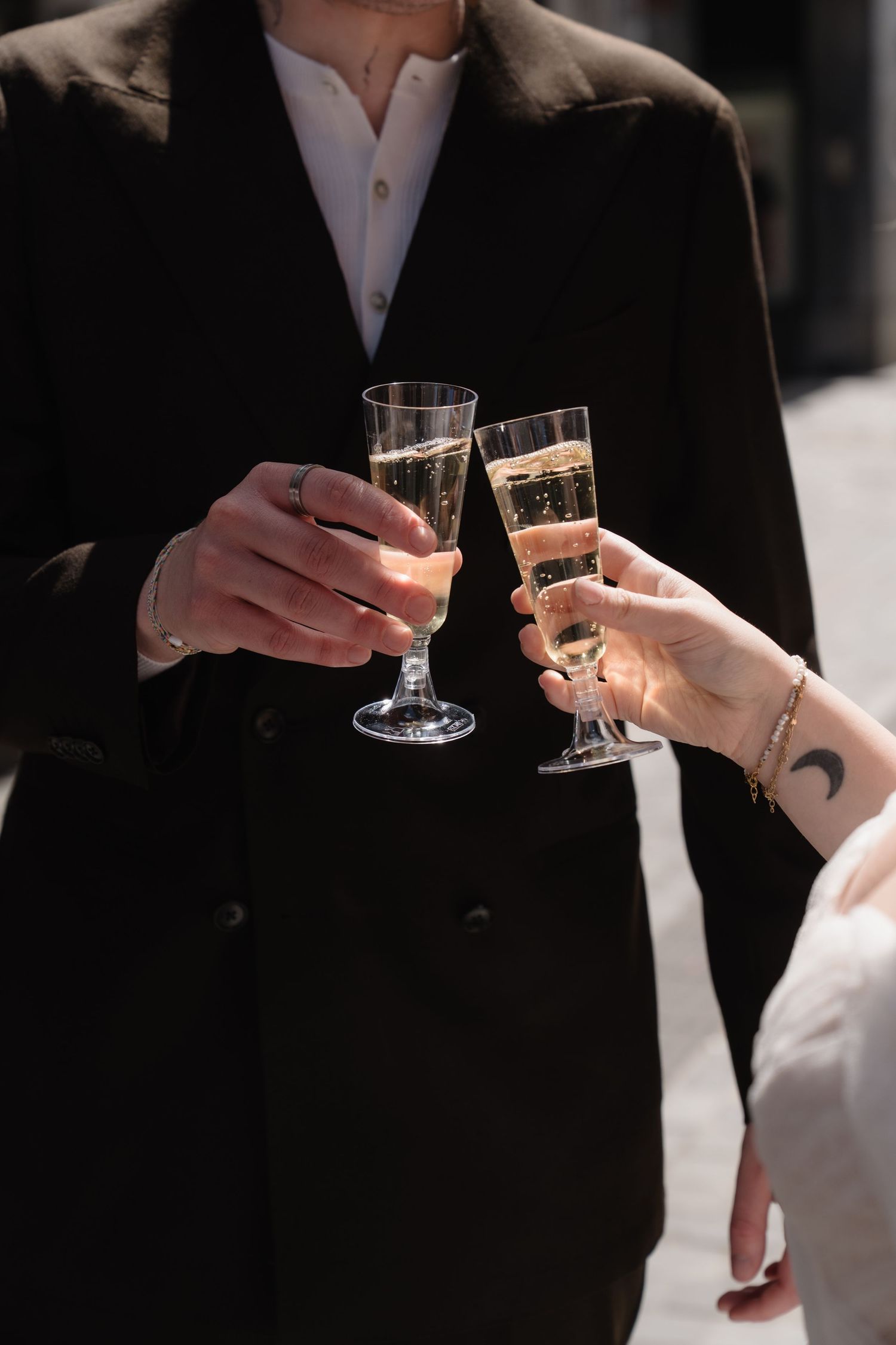 Bride and groom clinking champagne glasses outdoors, celebrating their wedding day in elegant attire.
