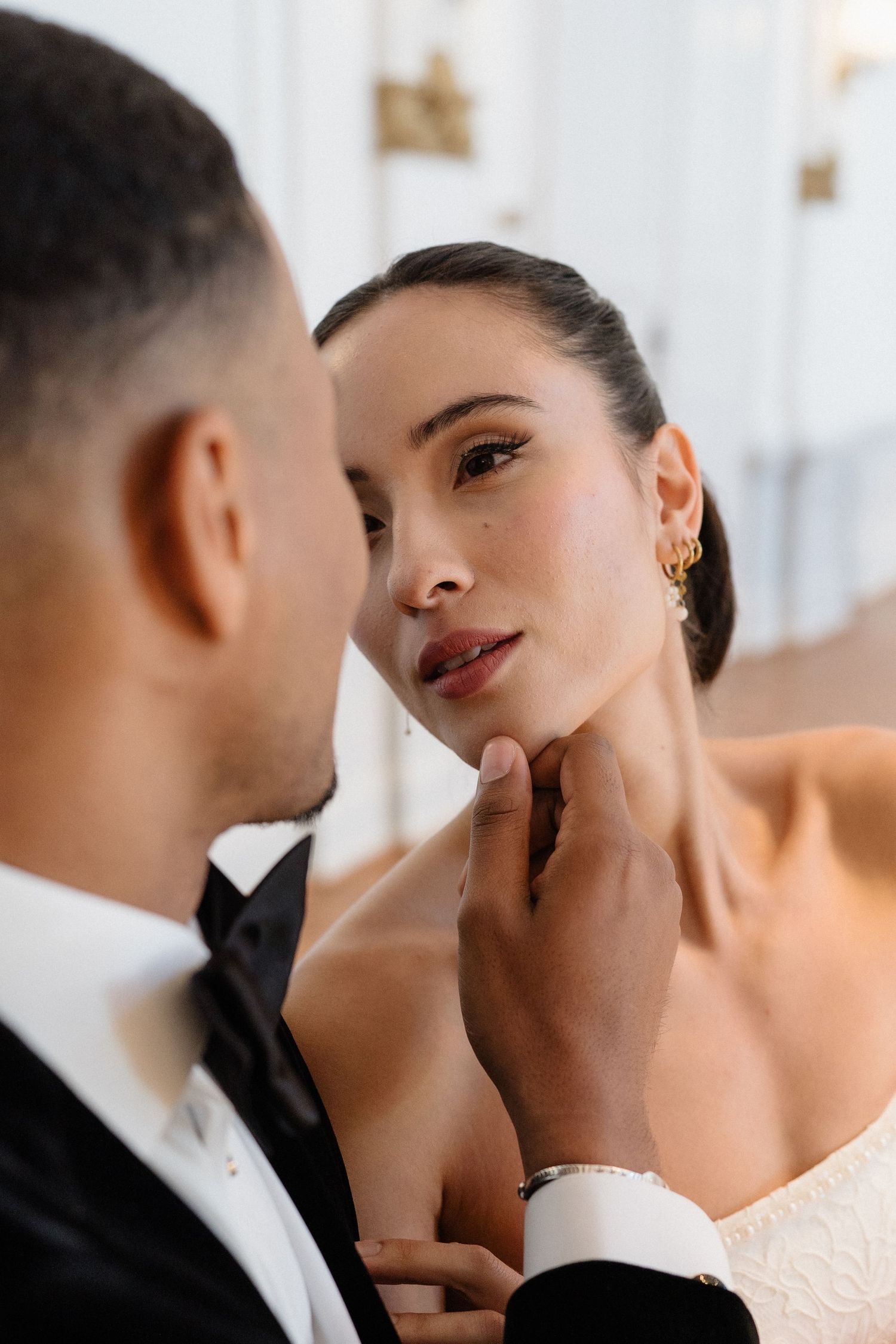 Groom tenderly lifting bride's chin as she gazes at him in elegant wedding attire.