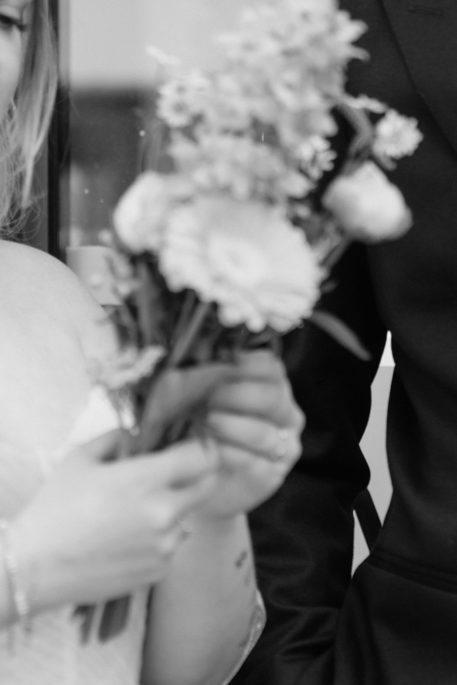 Black and white close-up of bride and groom holding a delicate floral bouquet together at wedding.