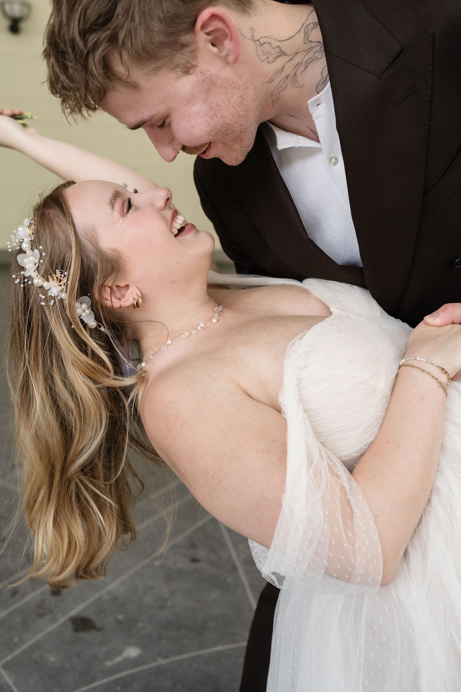 Laughing bride leaning back joyfully as groom leans in close during romantic wedding day moment.