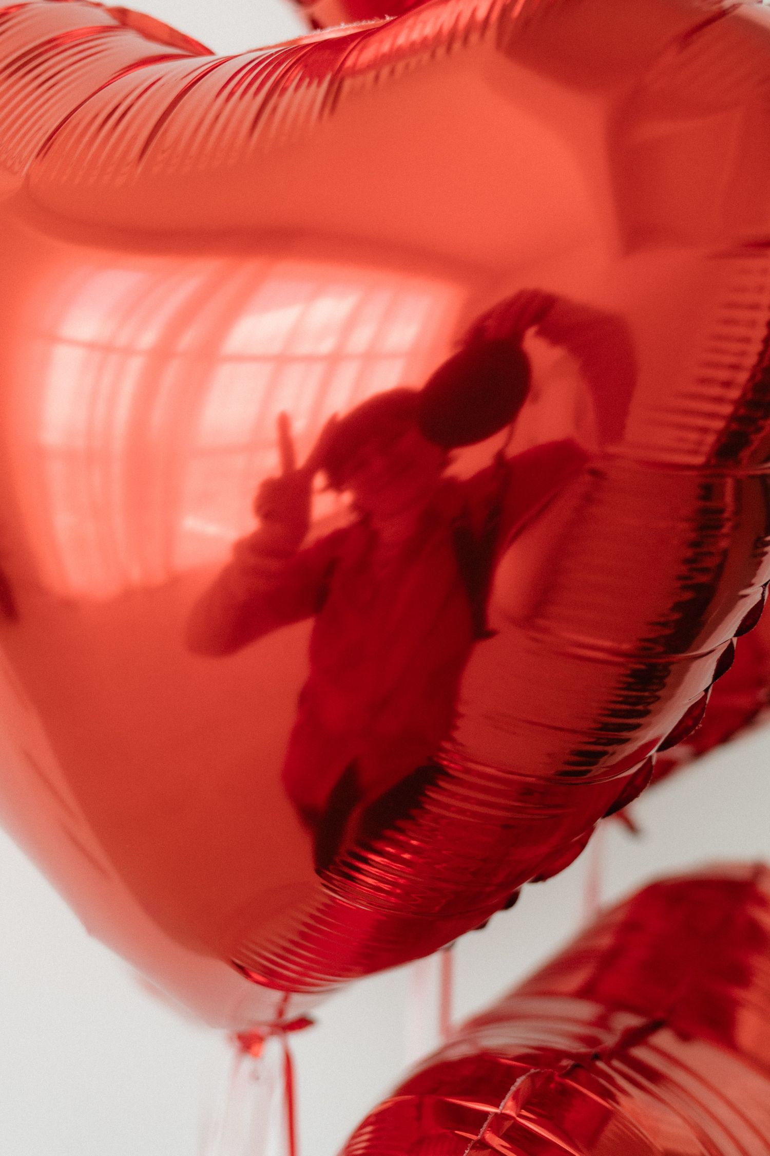 Close-up of shiny red heart-shaped foil balloon with reflection of person holding camera visible on surface.