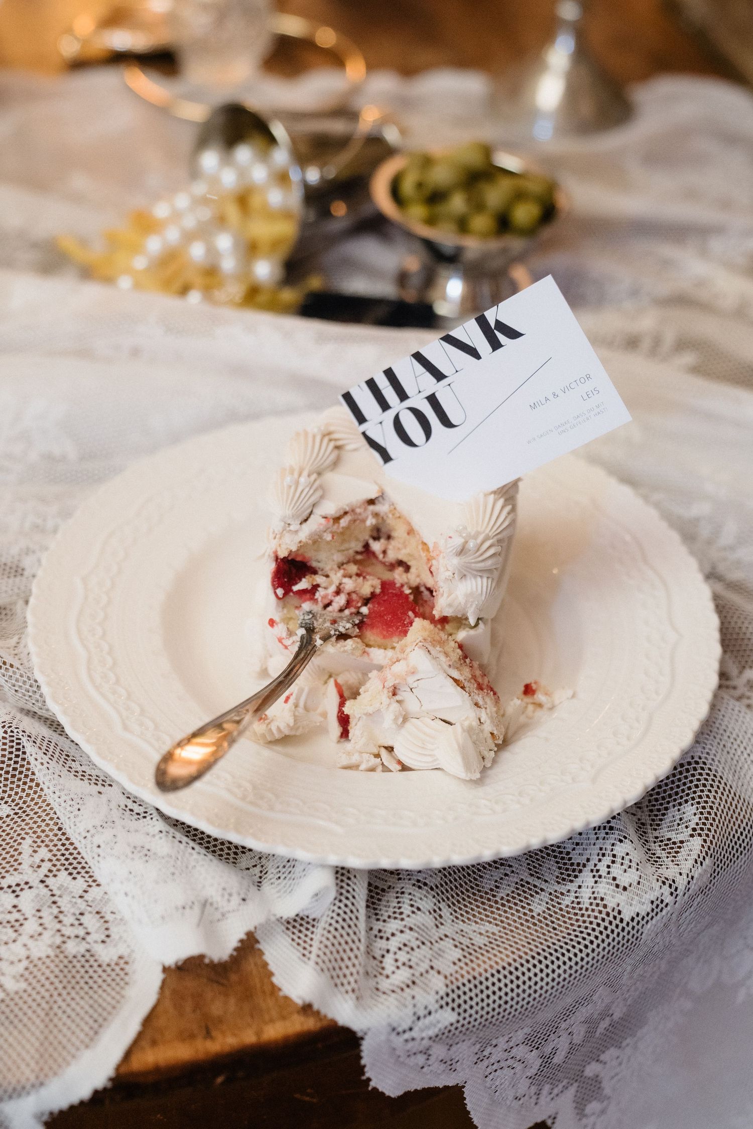 Elegant wedding place setting with a slice of cake and a thank you card on a white lace tablecloth.