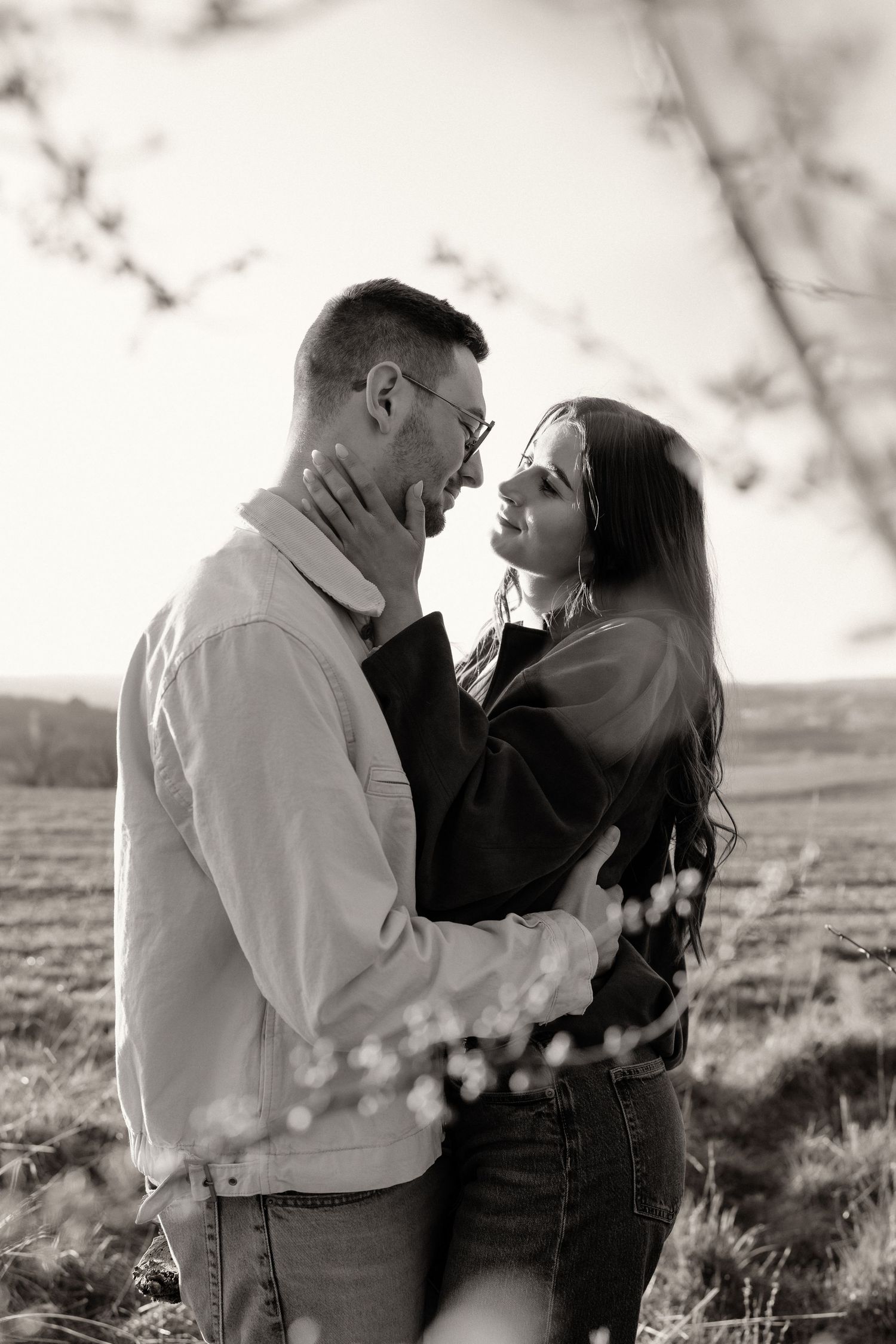 Black and white photo of a couple embracing in a field, woman touching mans face tenderly.