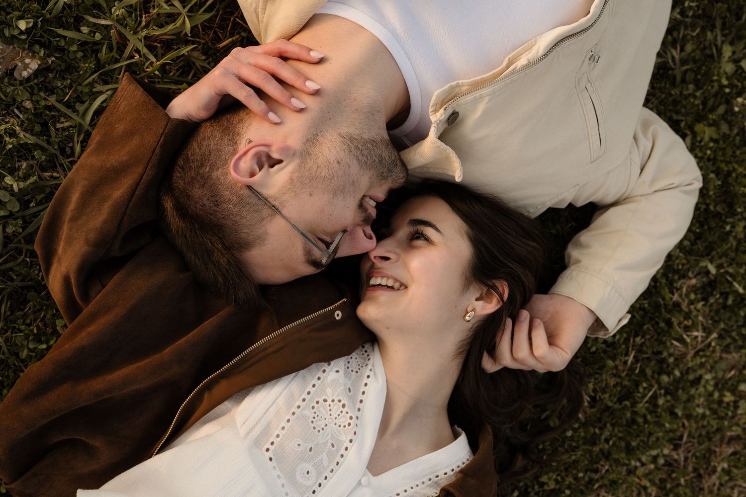 Overhead view of couple lying on grass, smiling and leaning in for a kiss together.
