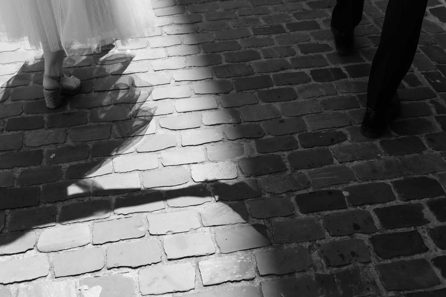 Black and white artistic photo of bride and groom shadows cast on cobblestone pavement.
