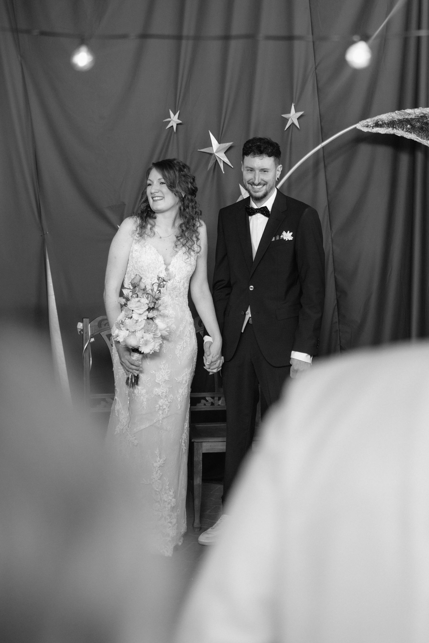 Black and white photo of smiling bride and groom holding hands at wedding ceremony with star decorations.