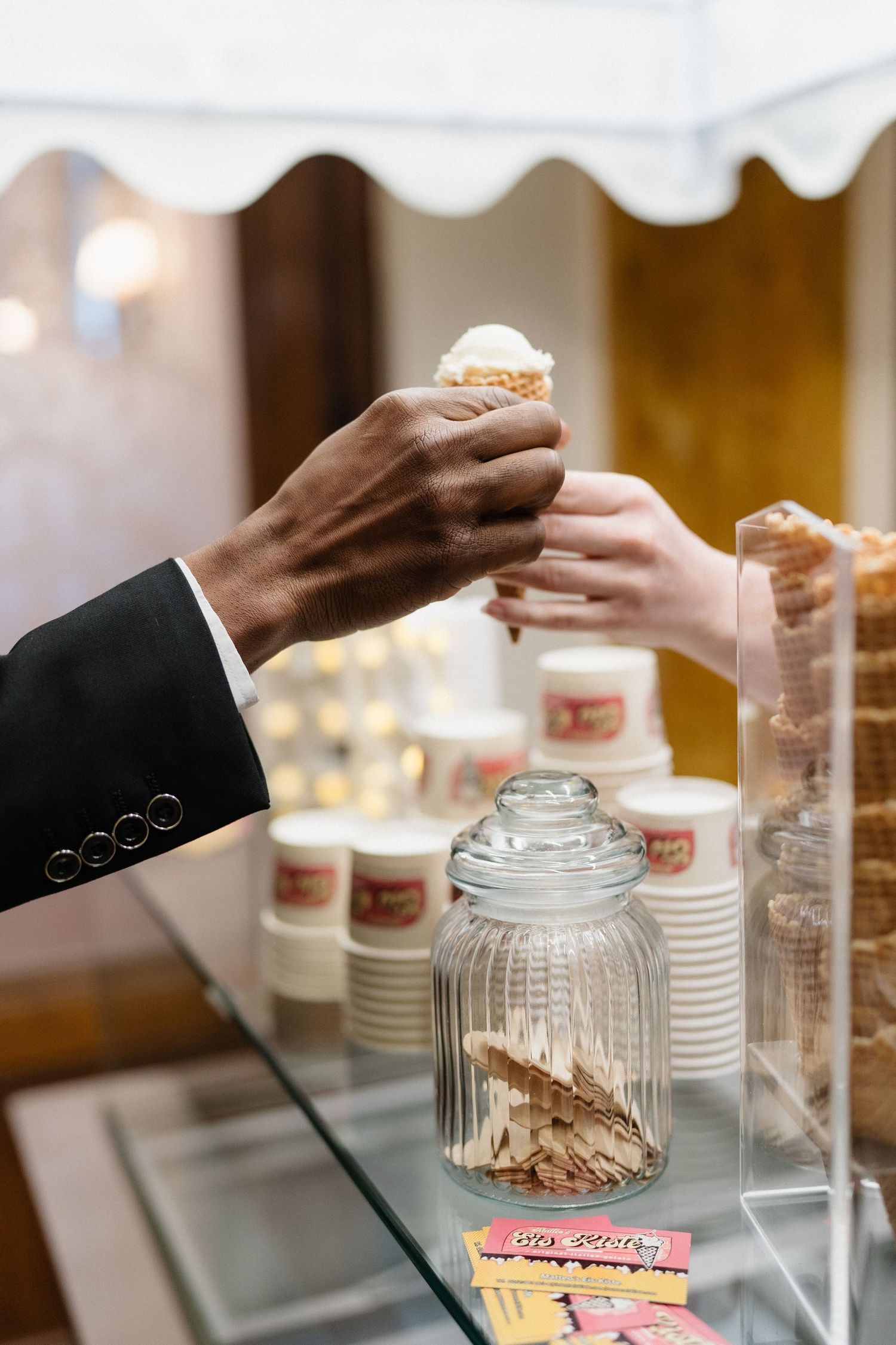 A person in a suit receives an ice cream cone at a dessert counter with stacked cups in the background.