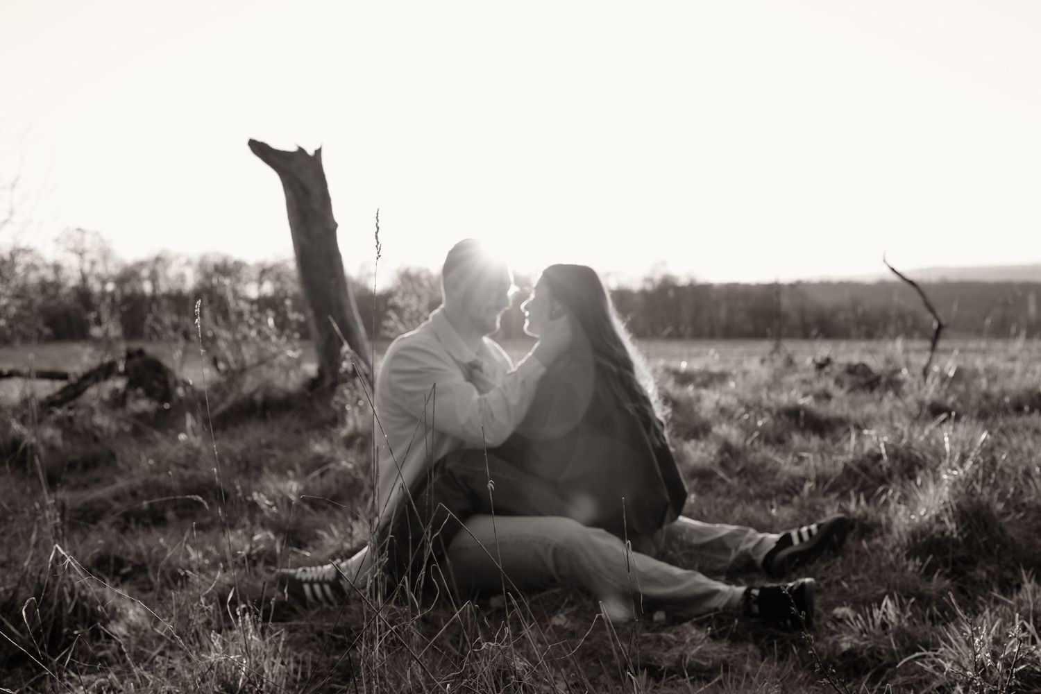 Romantic couple sitting close together in a field at sunset in artistic black and white photo.
