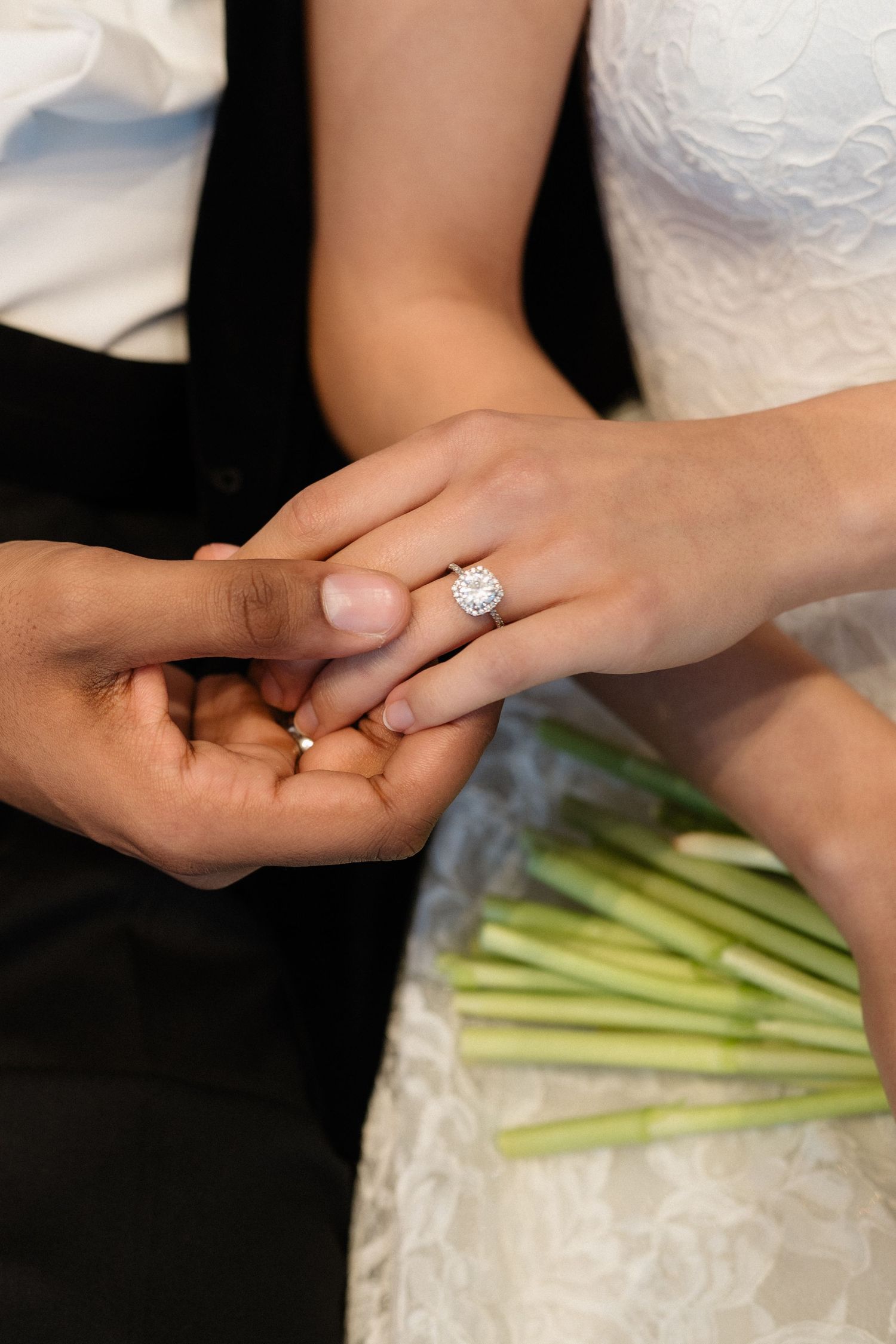 Close-up of bride's hand with diamond engagement ring held by groom during wedding ceremony.