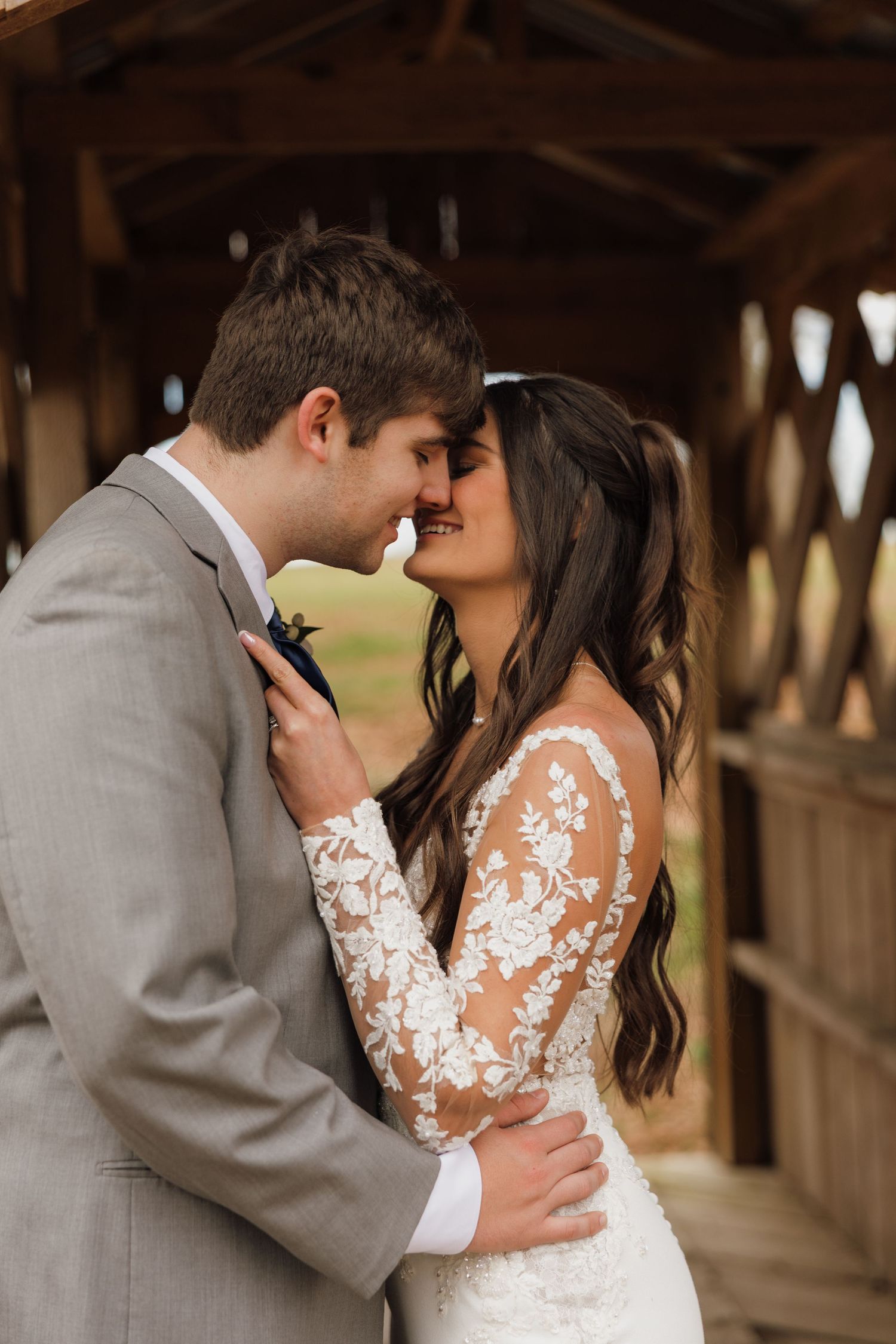 Romantic wedding couple embracing in a rustic wooden covered bridge setting.