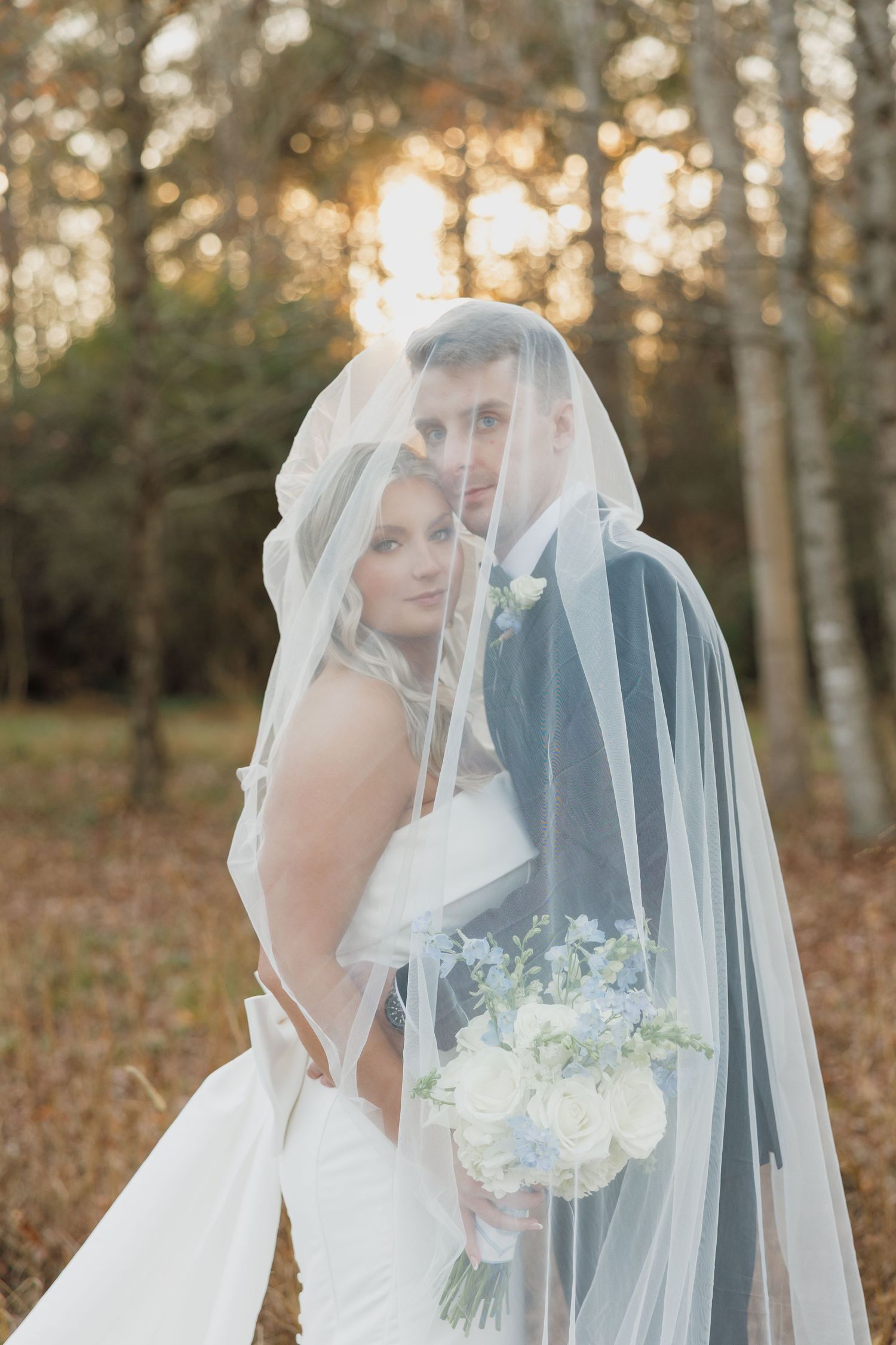 Romantic bridal portraits with flowing veil and white bouquet in natural woodland setting.