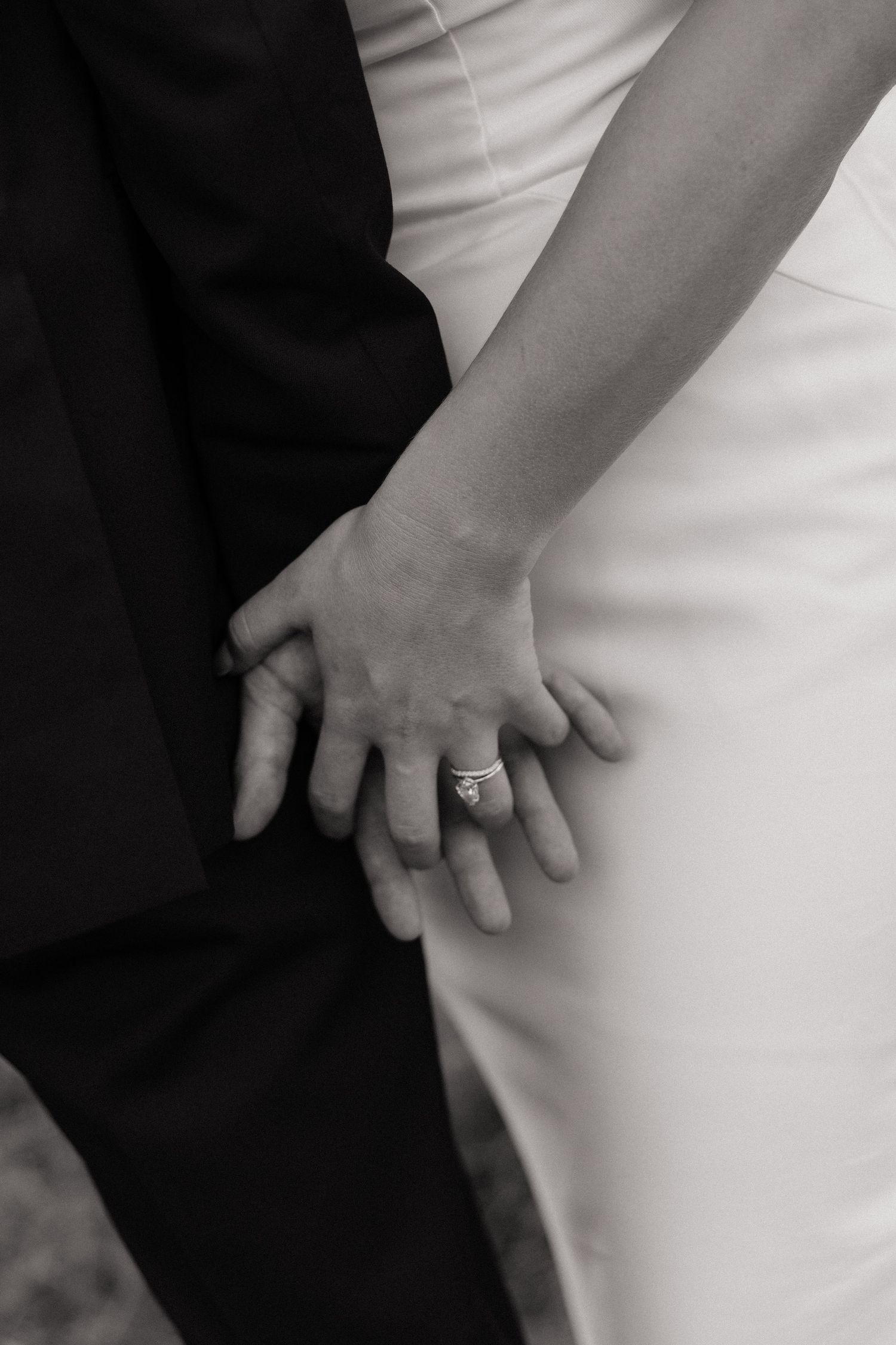 Close-up detail of wedding attire showing hands and formal wear in black and white.