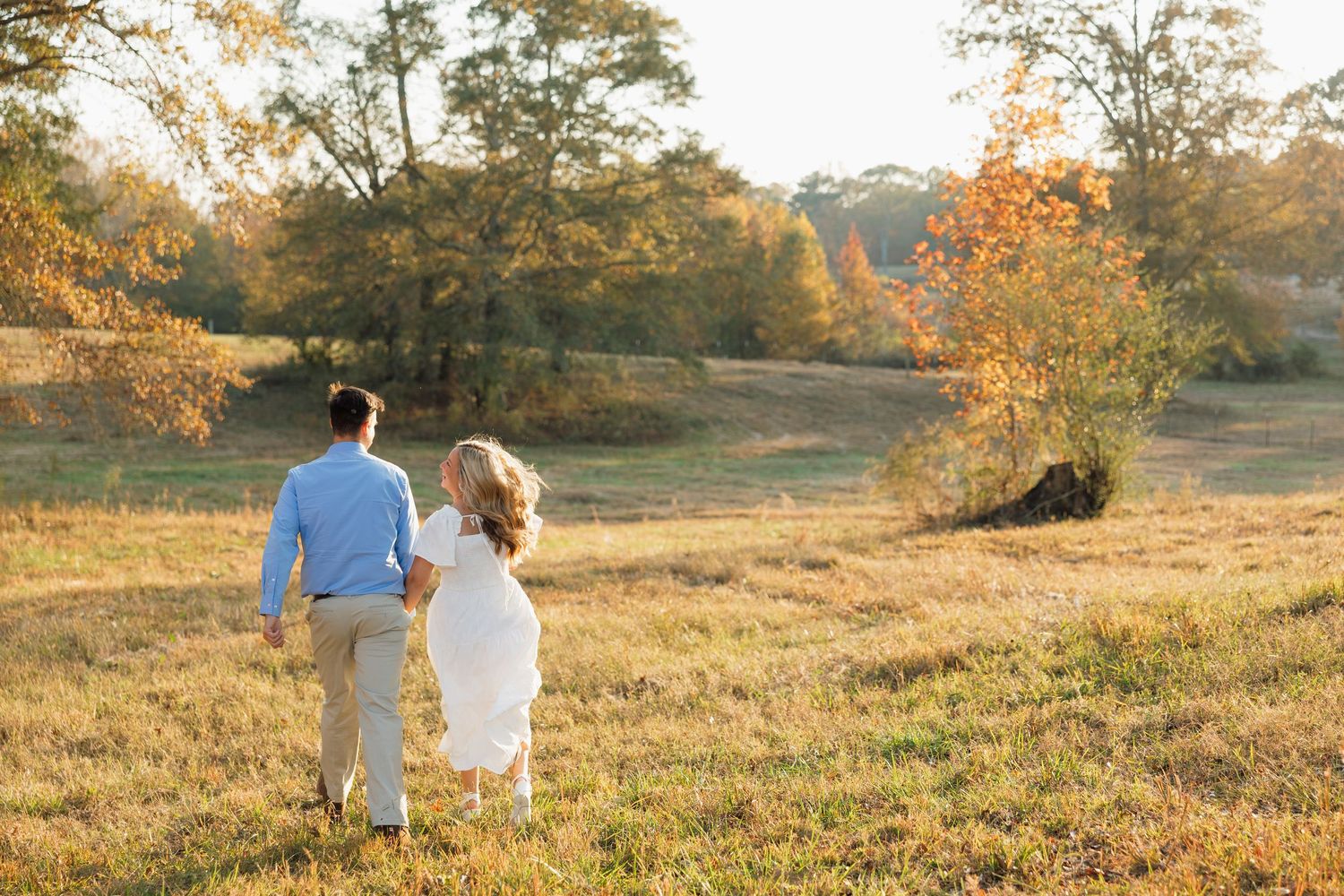 Couple walking together through a sun-drenched autumn field.