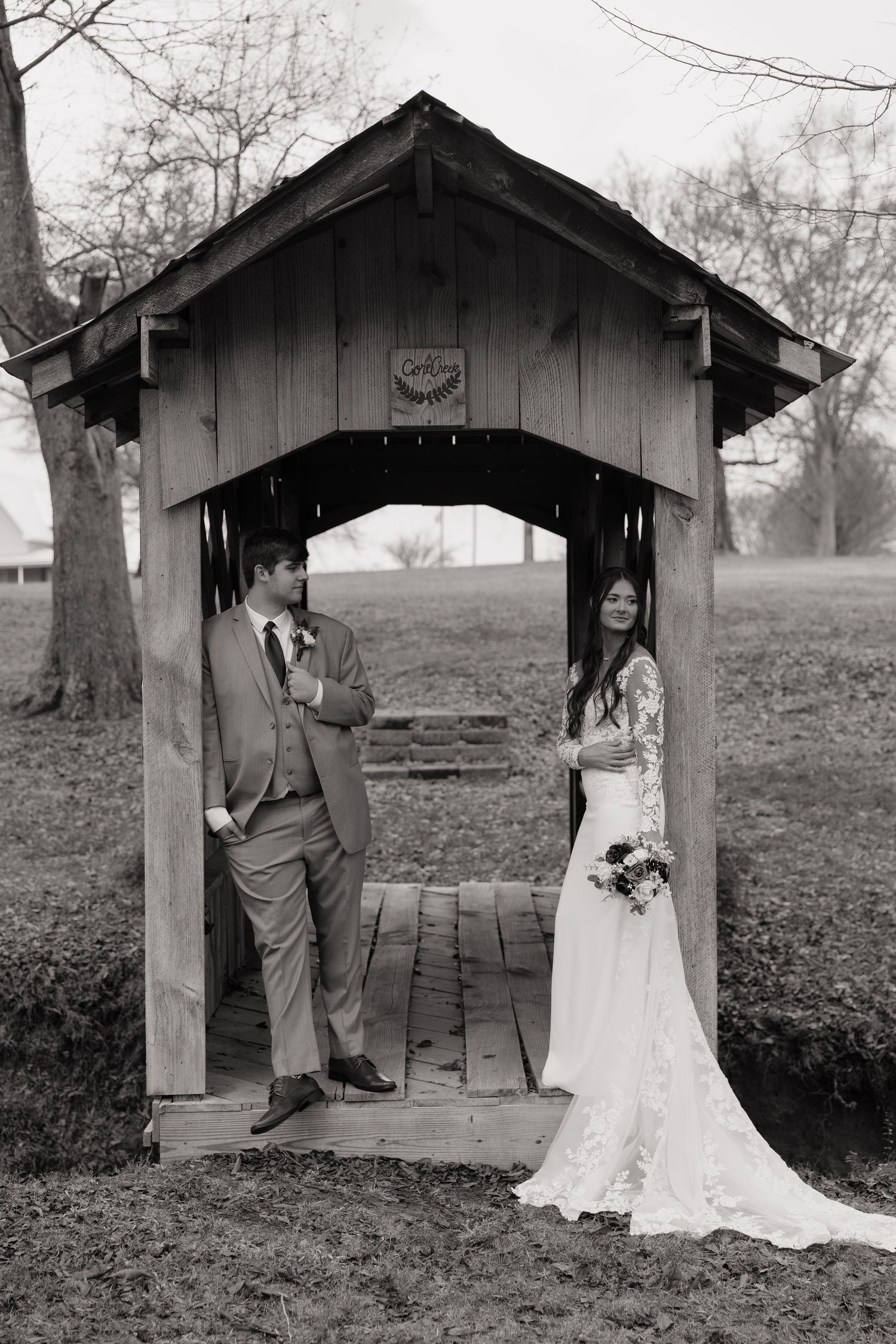 Black and white wedding photos taken under a rustic wooden shelter in a pastoral setting.