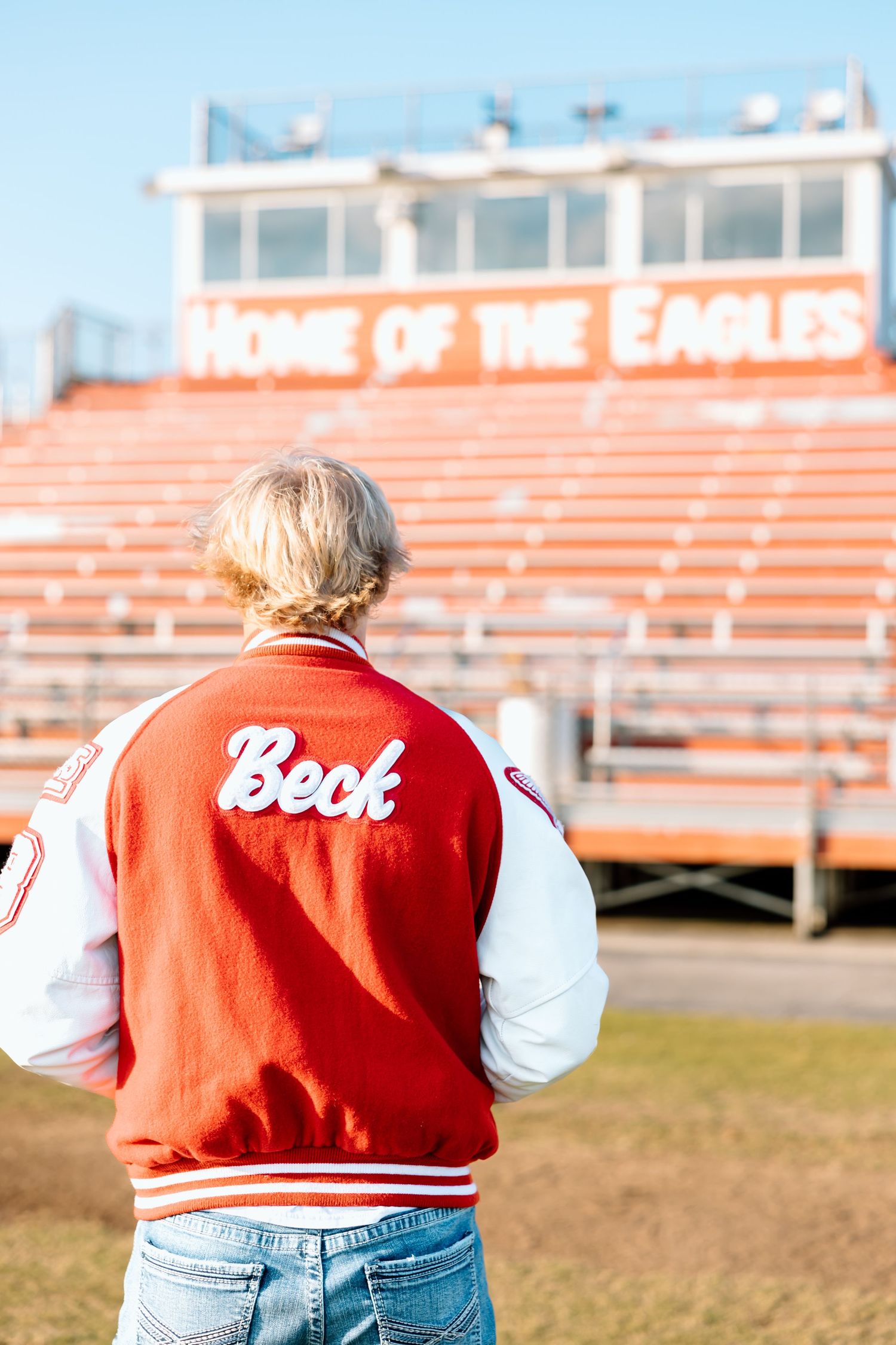 Back view of person wearing red and white varsity jacket at football stadium with Eagles bleachers.
