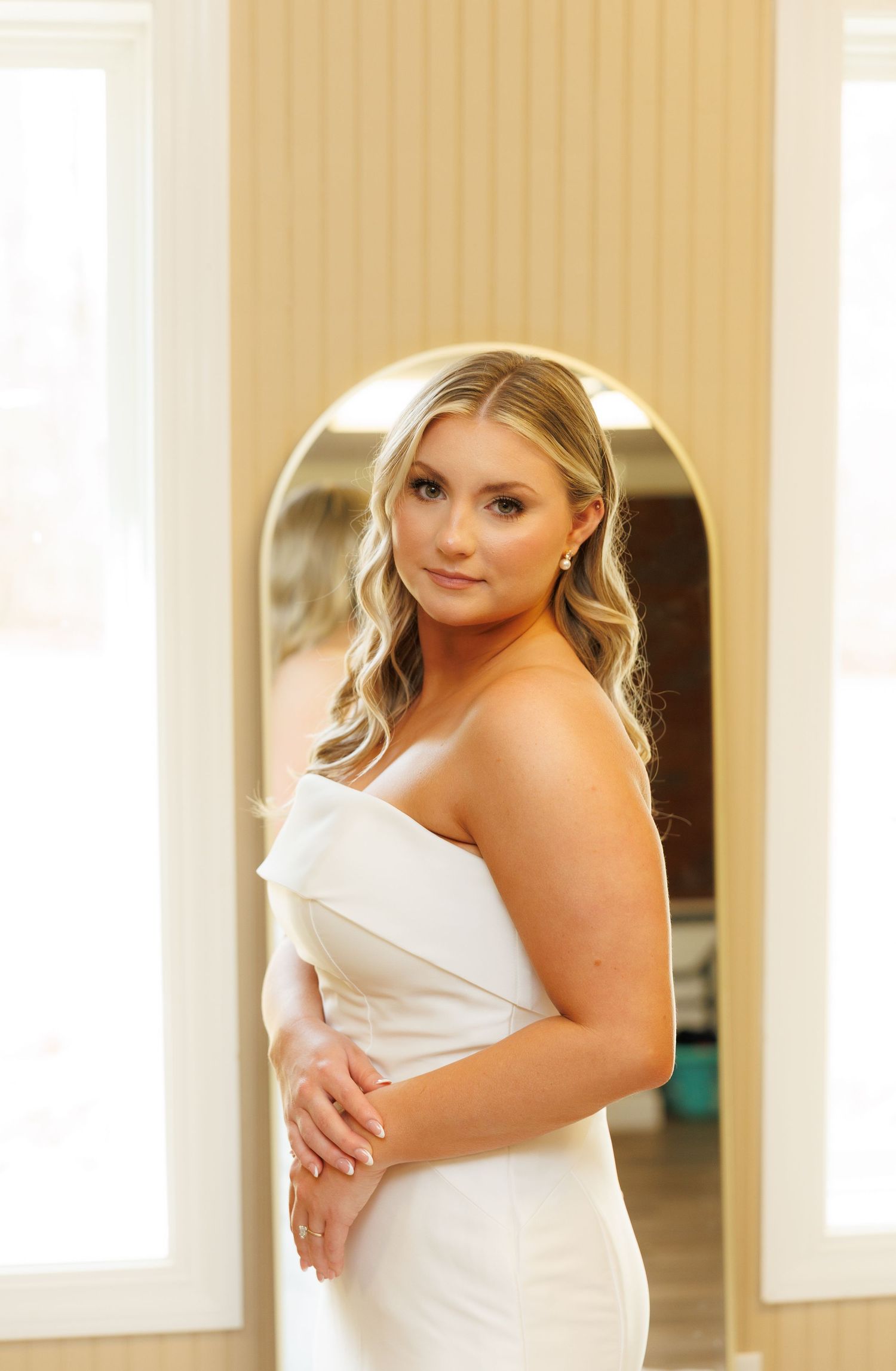 A person wearing a white dress poses gracefully in a sunlit room with warm beige walls.