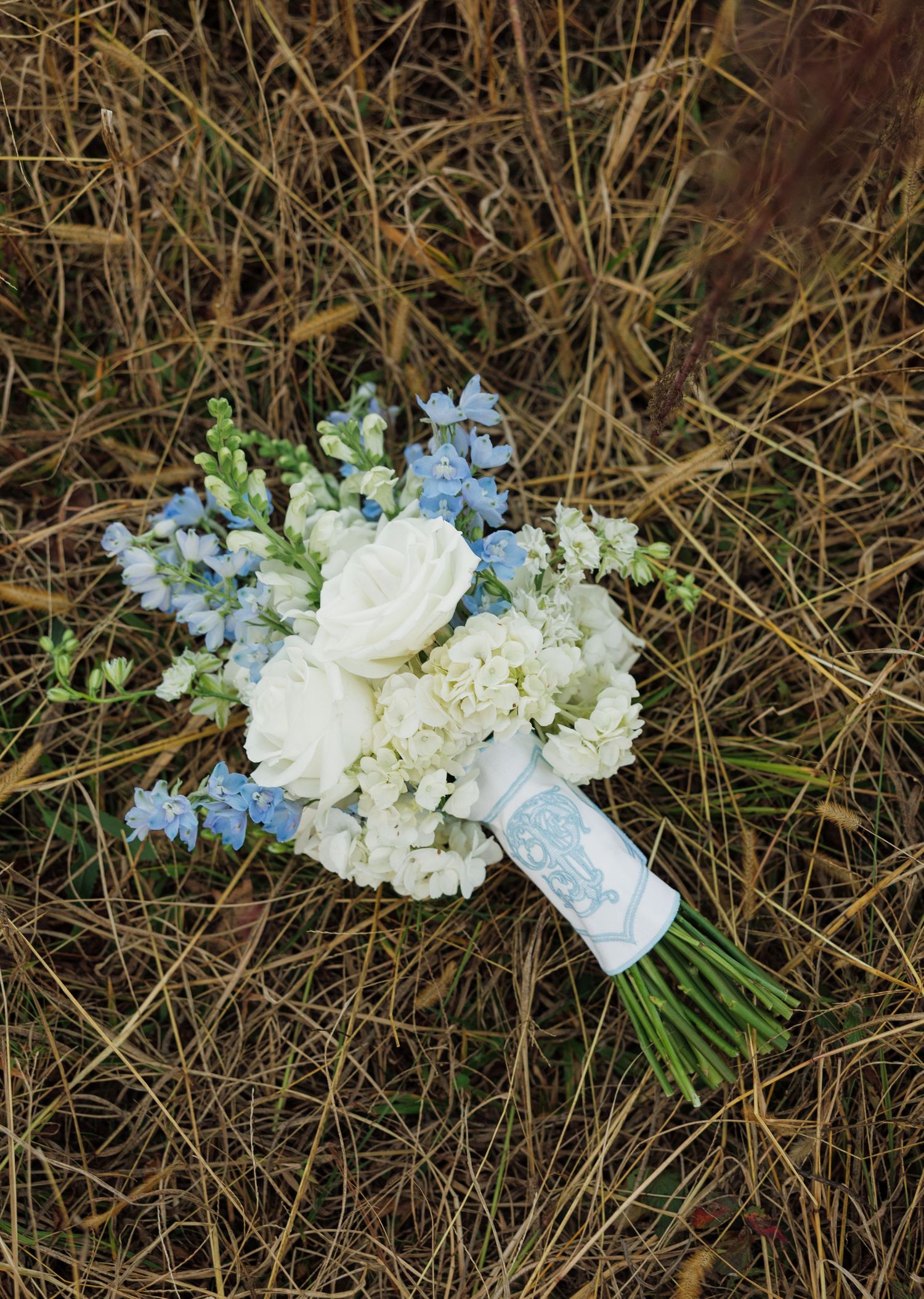 Wedding bouquet with white hydrangeas and blue flowers laying on dried grass.