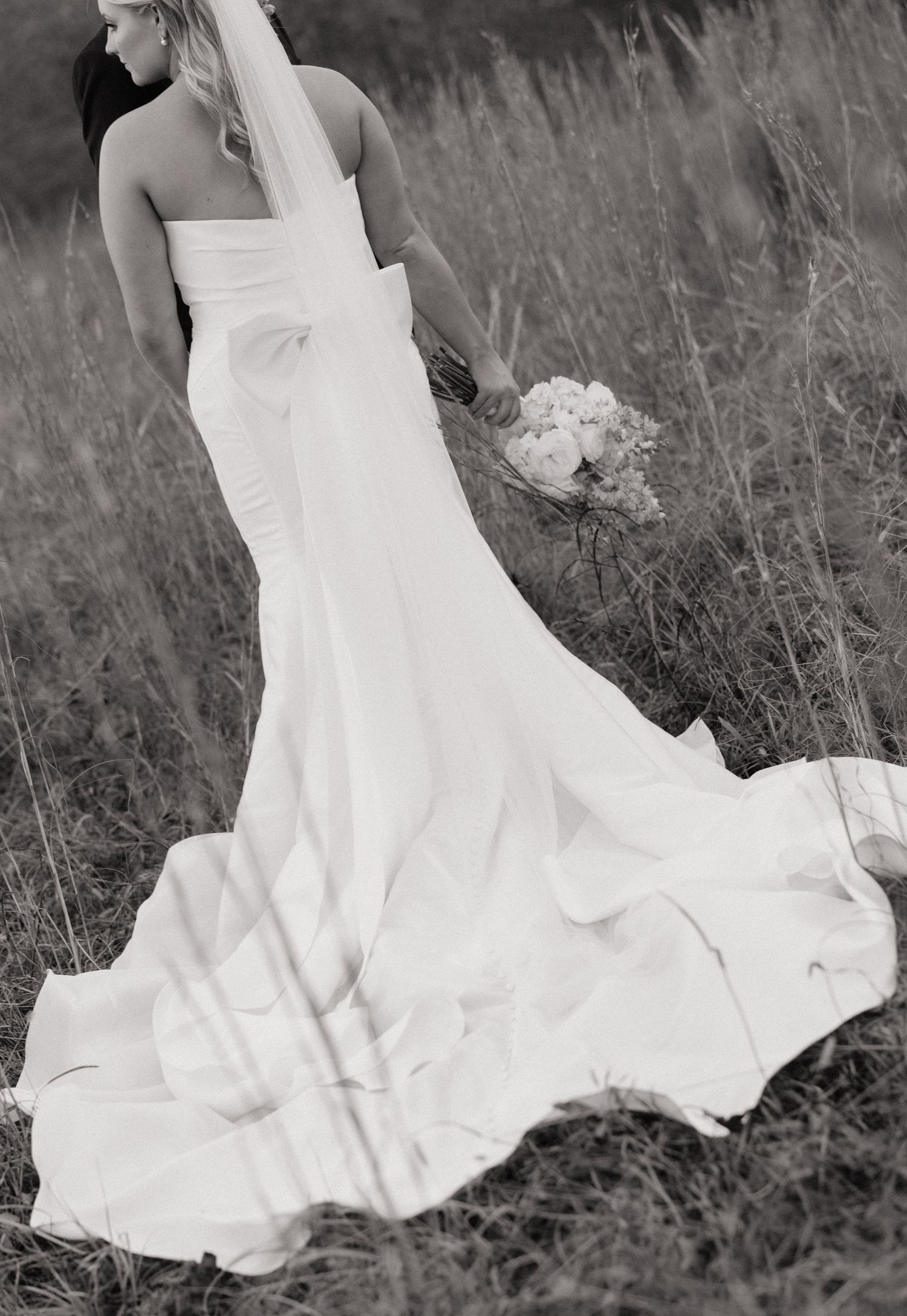 Black and white series of a flowing white wedding dress moving gracefully through tall grass in a field.