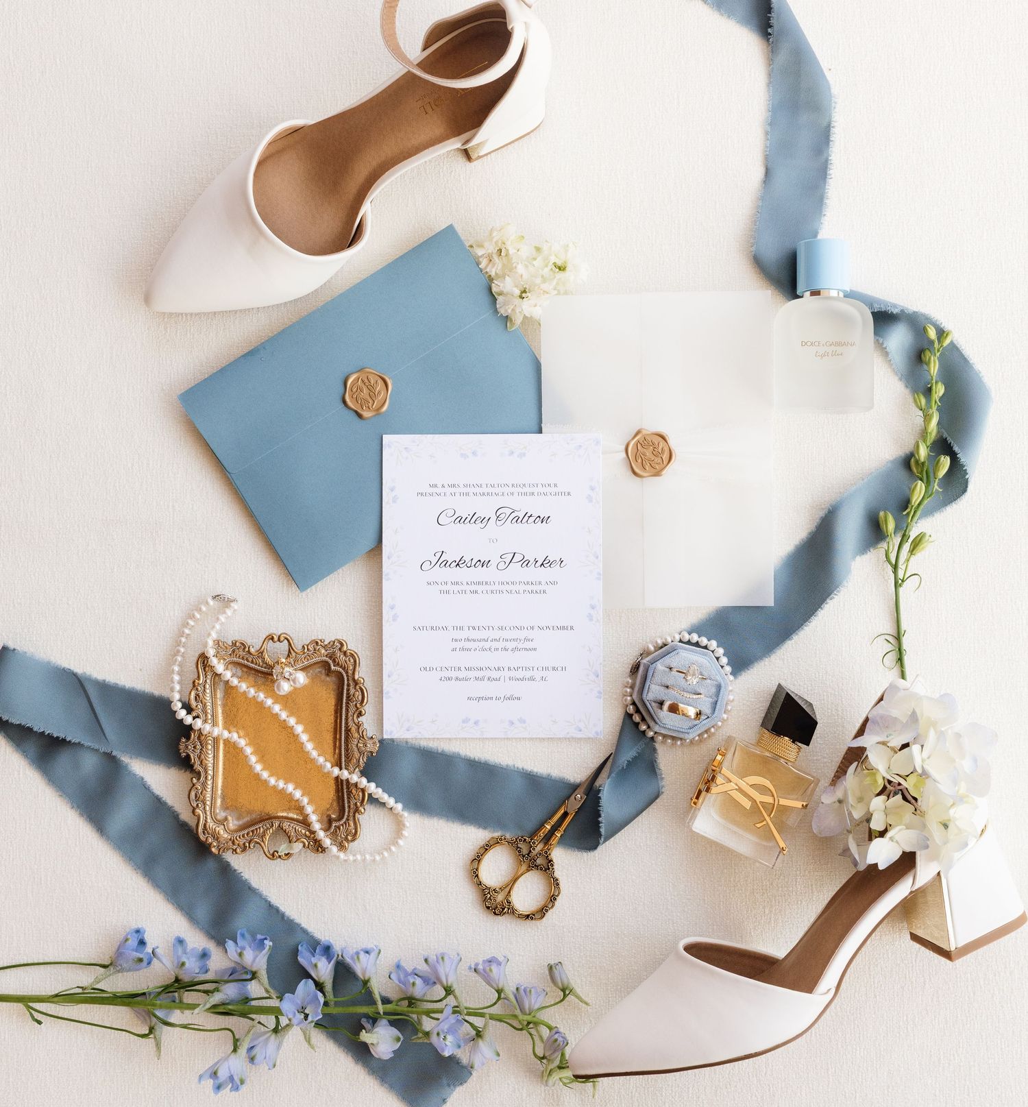 Wedding flat lay with blue silk ribbon, invitations, rings and delicate floral details.