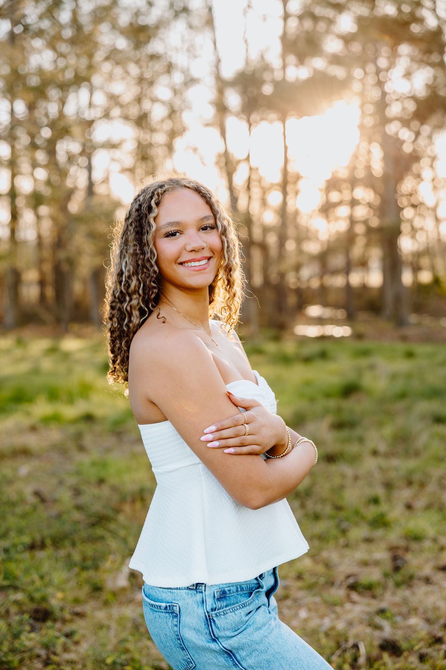 Outdoor portrait with sunlit trees in background and white top with jeans.