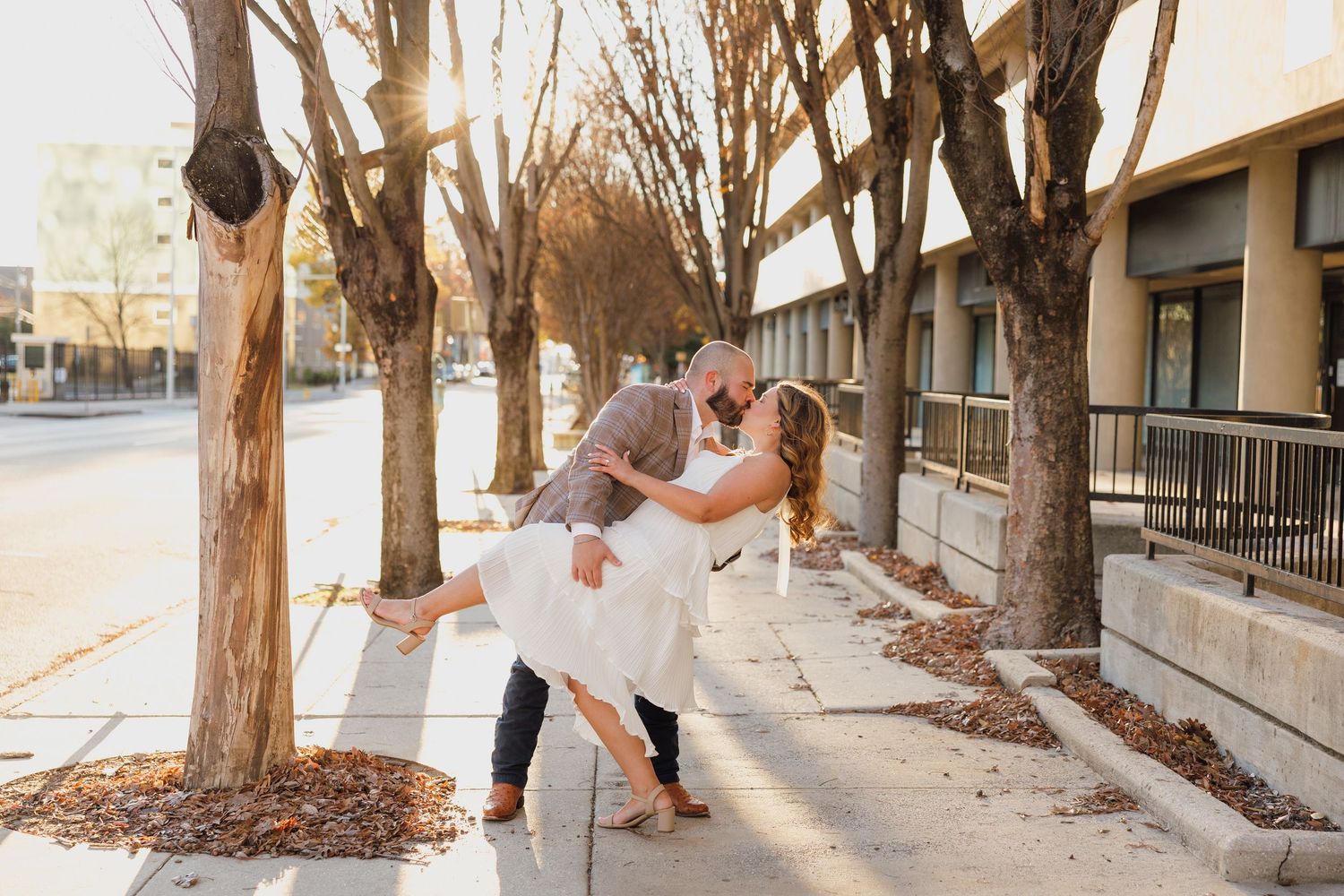 A couple walking along a tree-lined sidewalk on a sunny day.