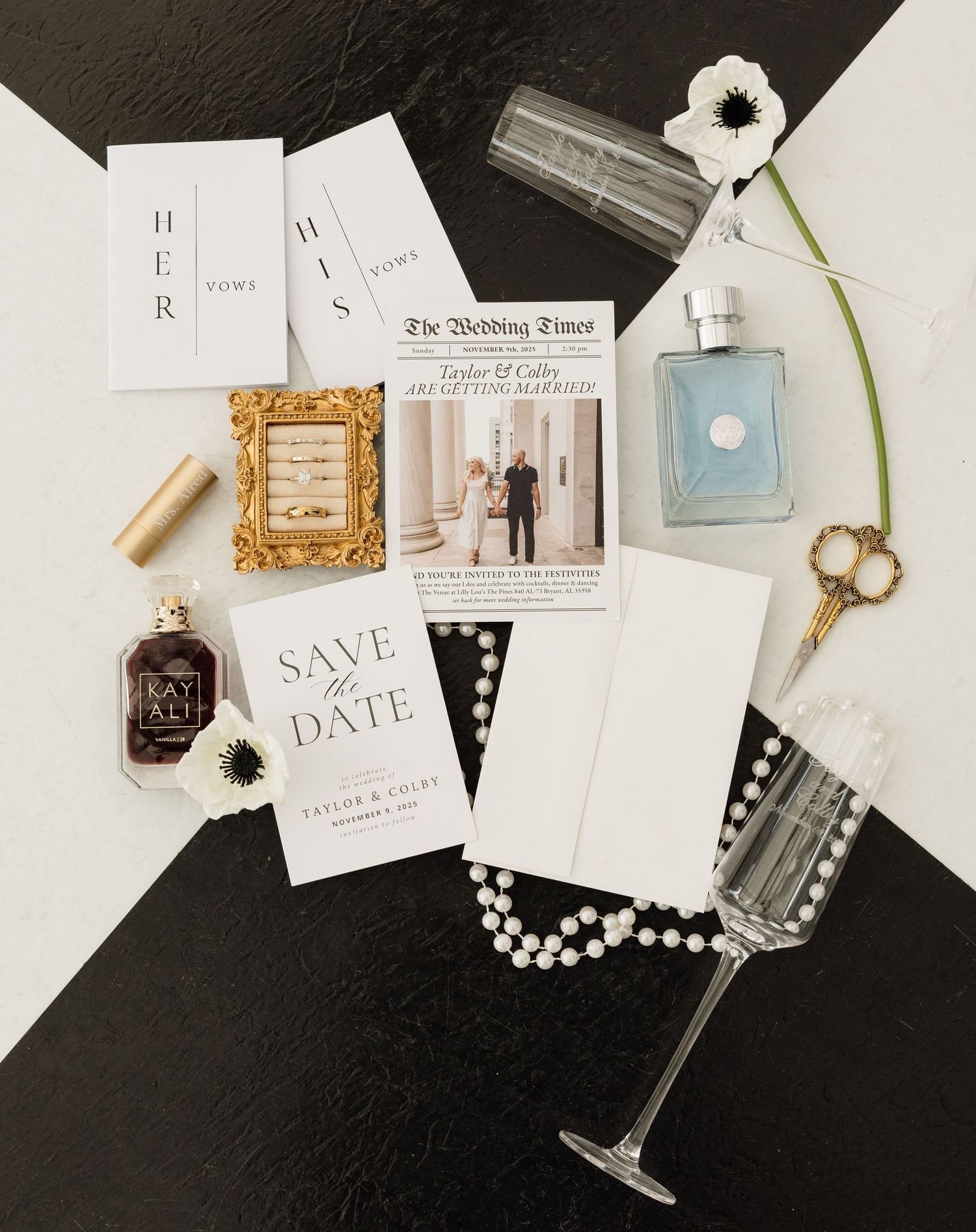 Wedding stationery flatlay with save the date cards, perfume bottle, champagne glass, pearls and decorative elements on black.