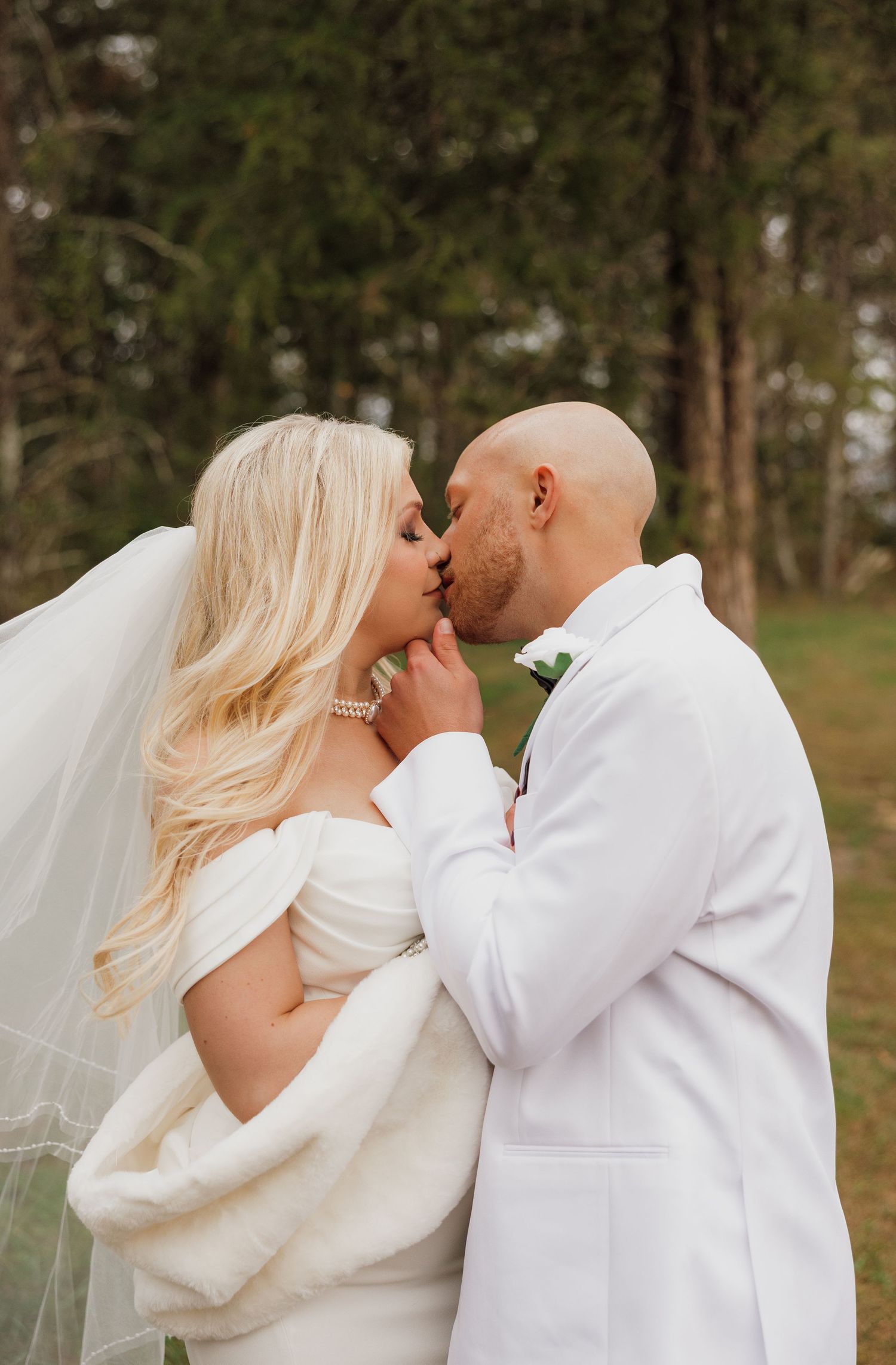 A series of romantic wedding photos showing a couple in white sharing intimate kisses outdoors among trees.