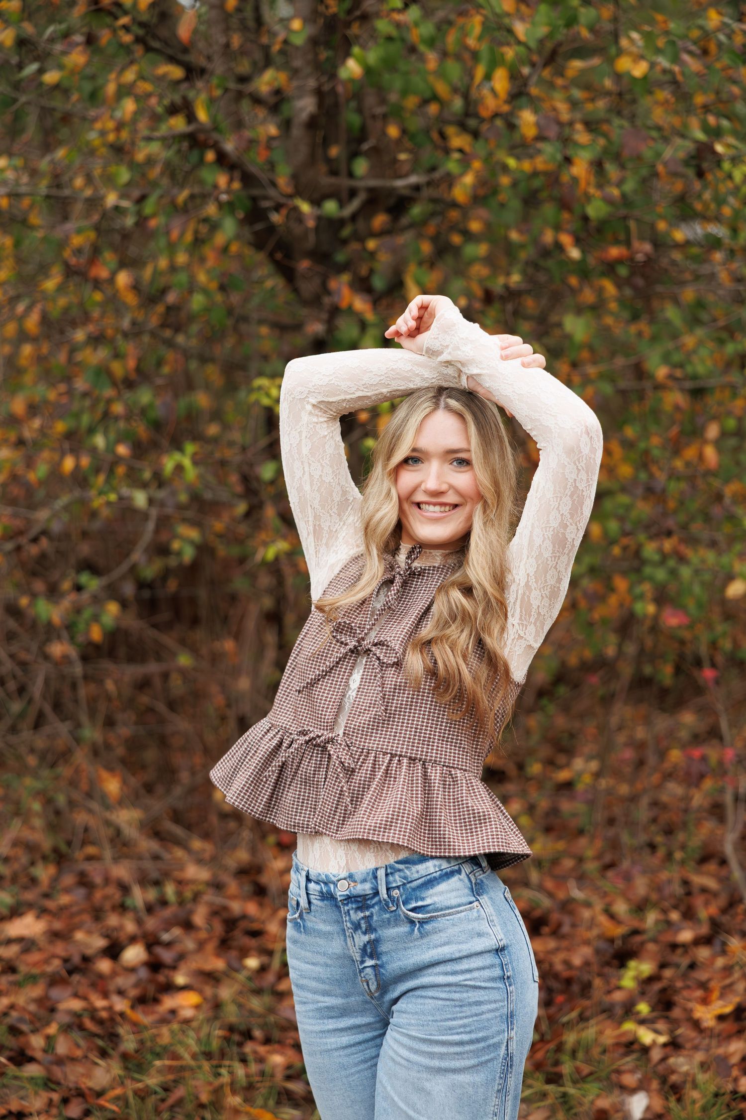 Autumn portrait of woman in ruffled top and jeans posing against fall foliage.