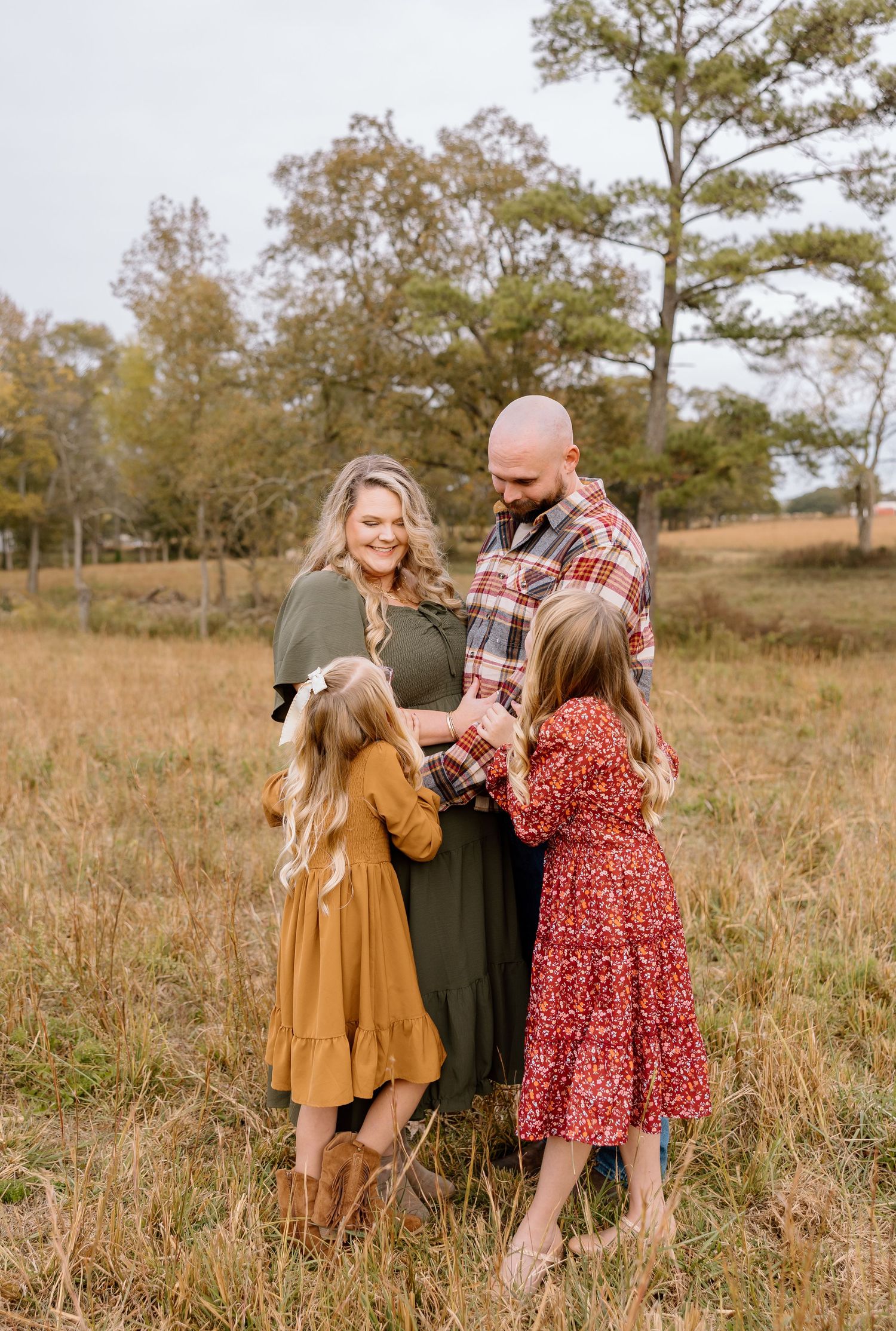 Family wearing autumn colored outfits plays together in a golden field at sunset.