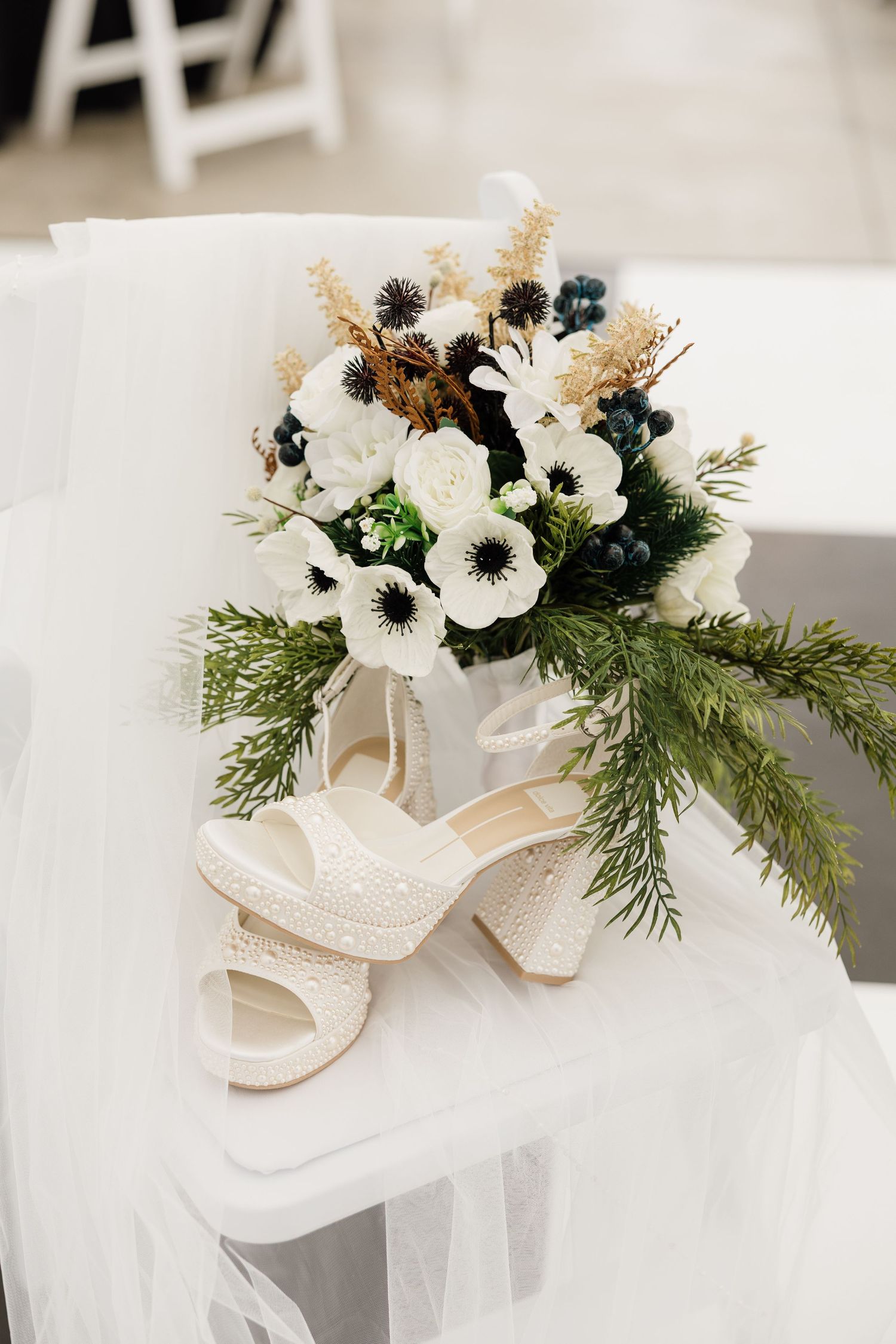 White wedding shoes decorated with winter greenery and delicate anemone flowers.