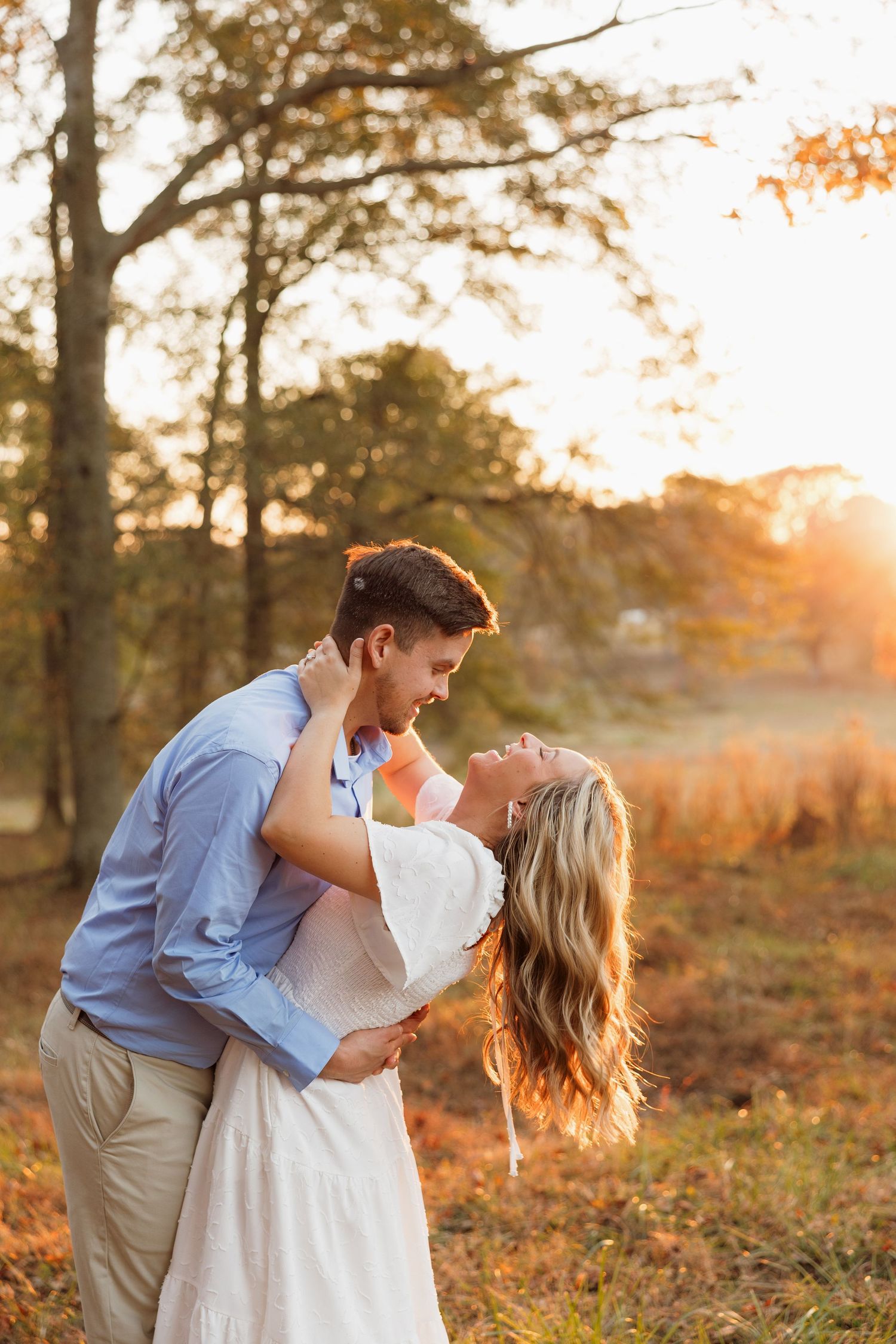 Romantic autumn engagement photo with golden sunset light through trees.