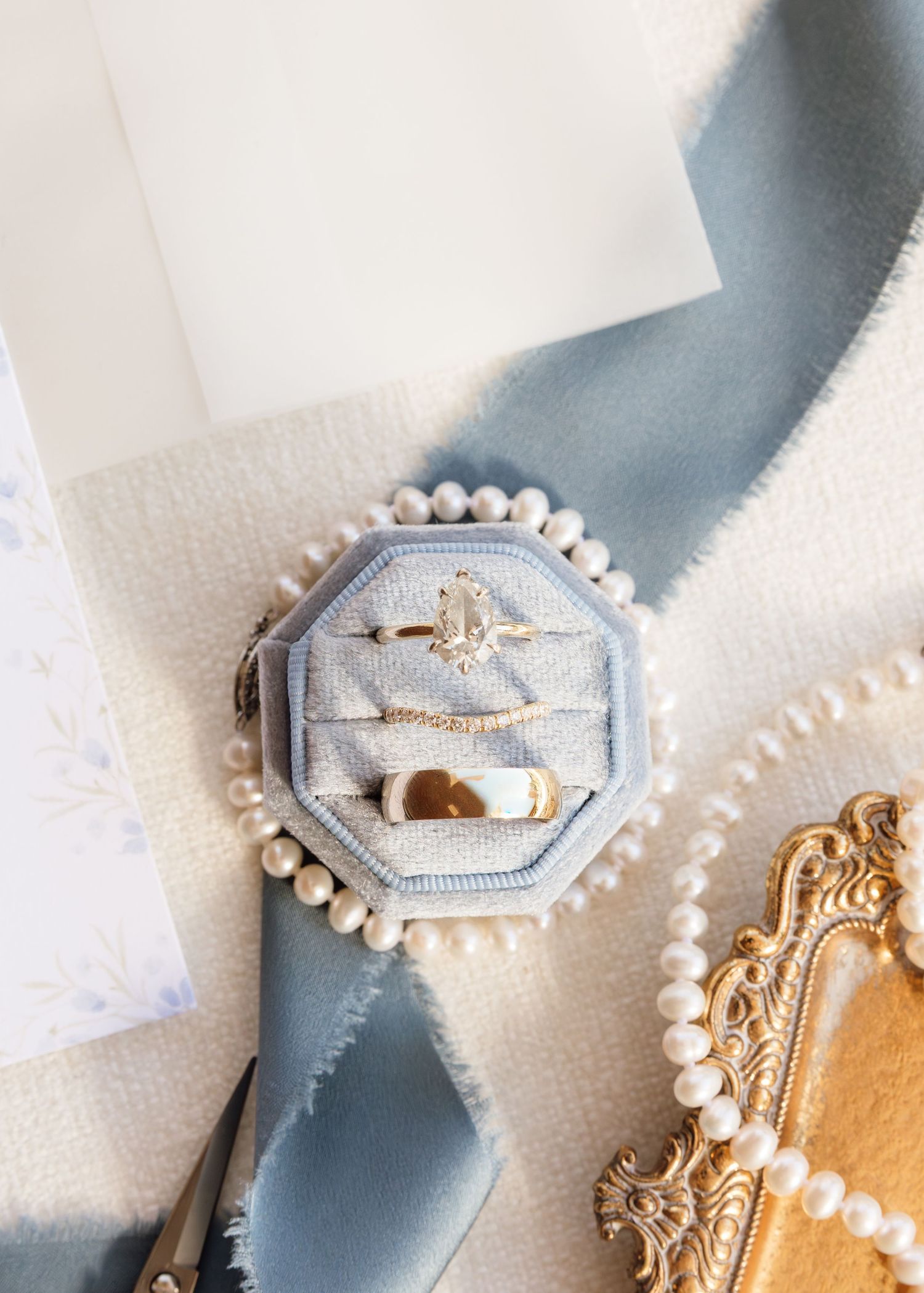 Elegant wedding rings and pearl jewelry arranged artistically on a light textured surface with soft shadows.