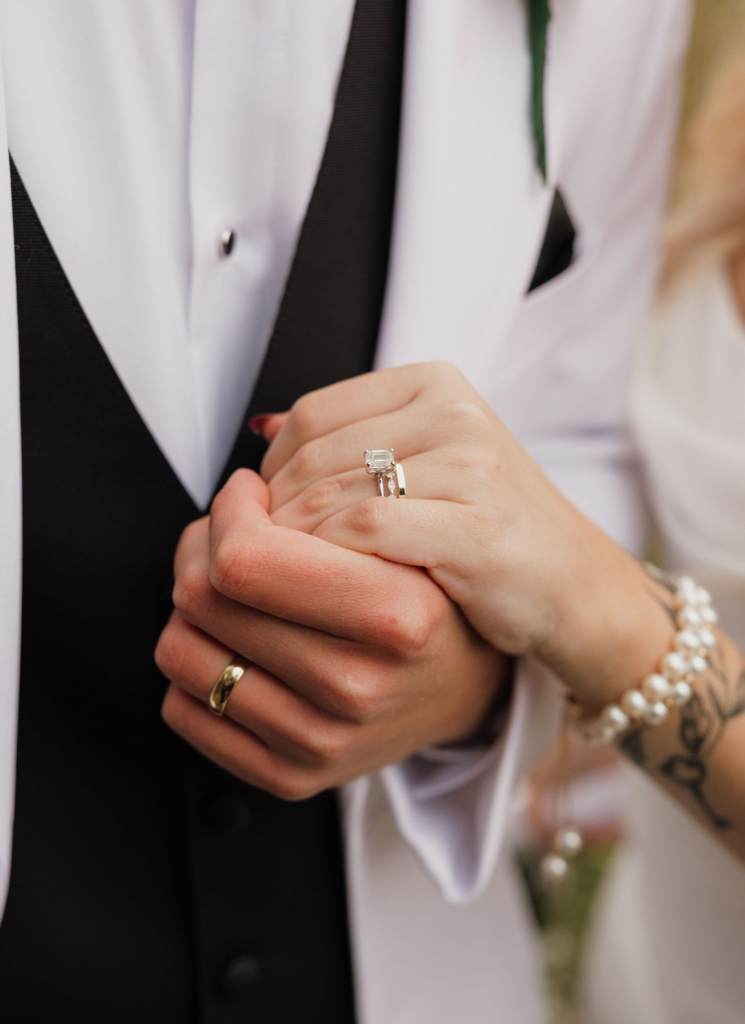 Close-up of newlyweds' hands showing wedding rings and formal attire details.