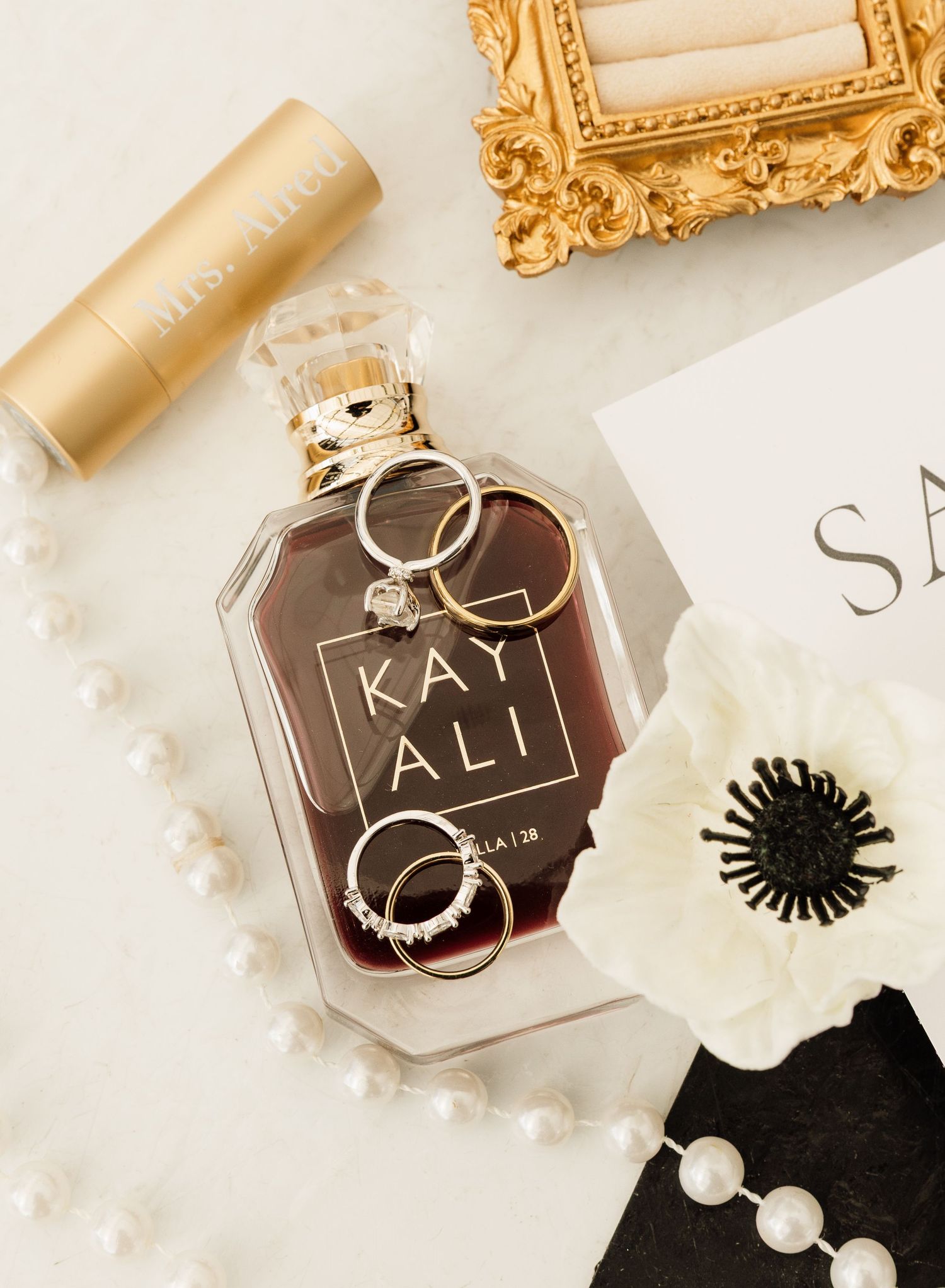 Elegant gold-framed glass perfume bottles with black and white pearl accessories displayed on a white surface.