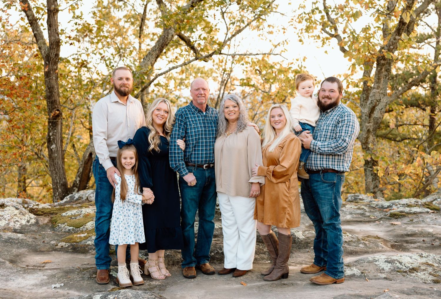 A group of people stand together for outdoor family portraits in a wooded autumn setting during golden hour.