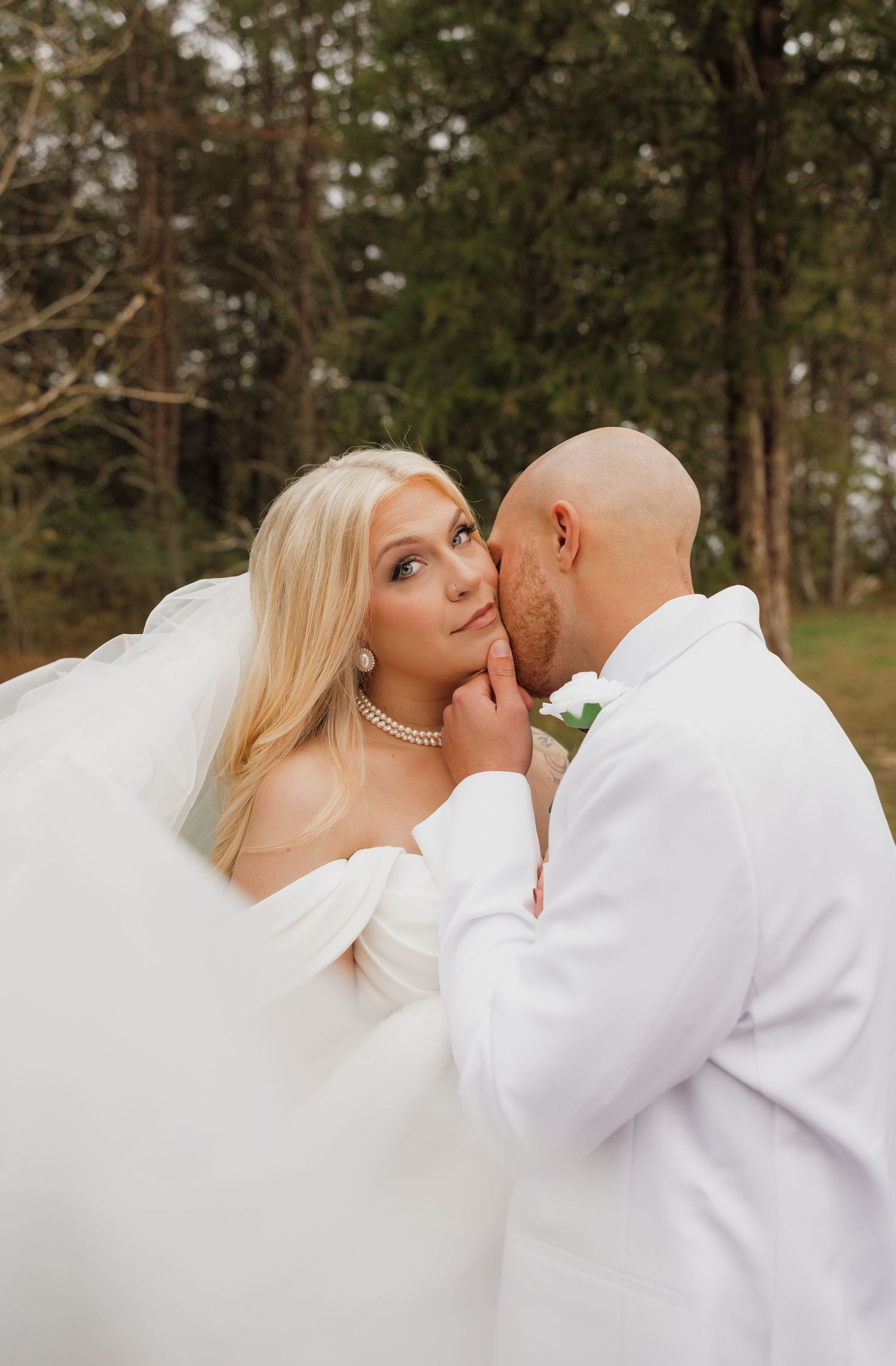 Romantic wedding couple sharing intimate moments in a wooded outdoor setting during golden hour.