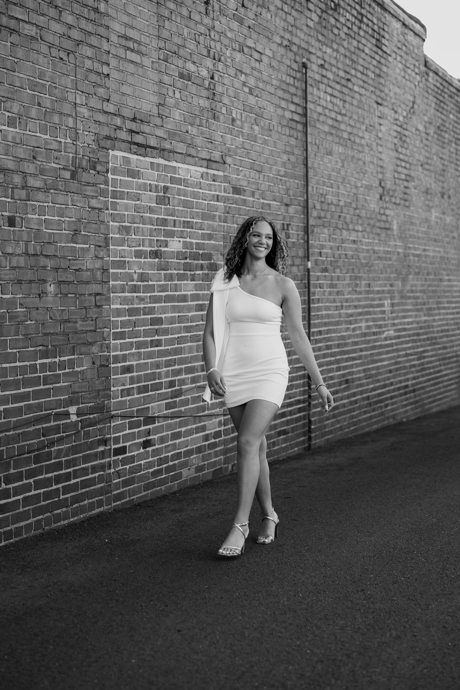Black and white portrait against brick wall wearing white dress.