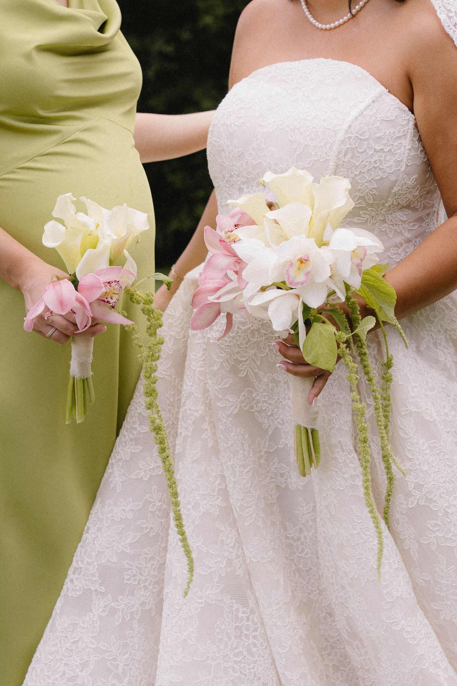 Bride and bridesmaid hold elegant white and pink calla lily bouquets with cascading greenery.