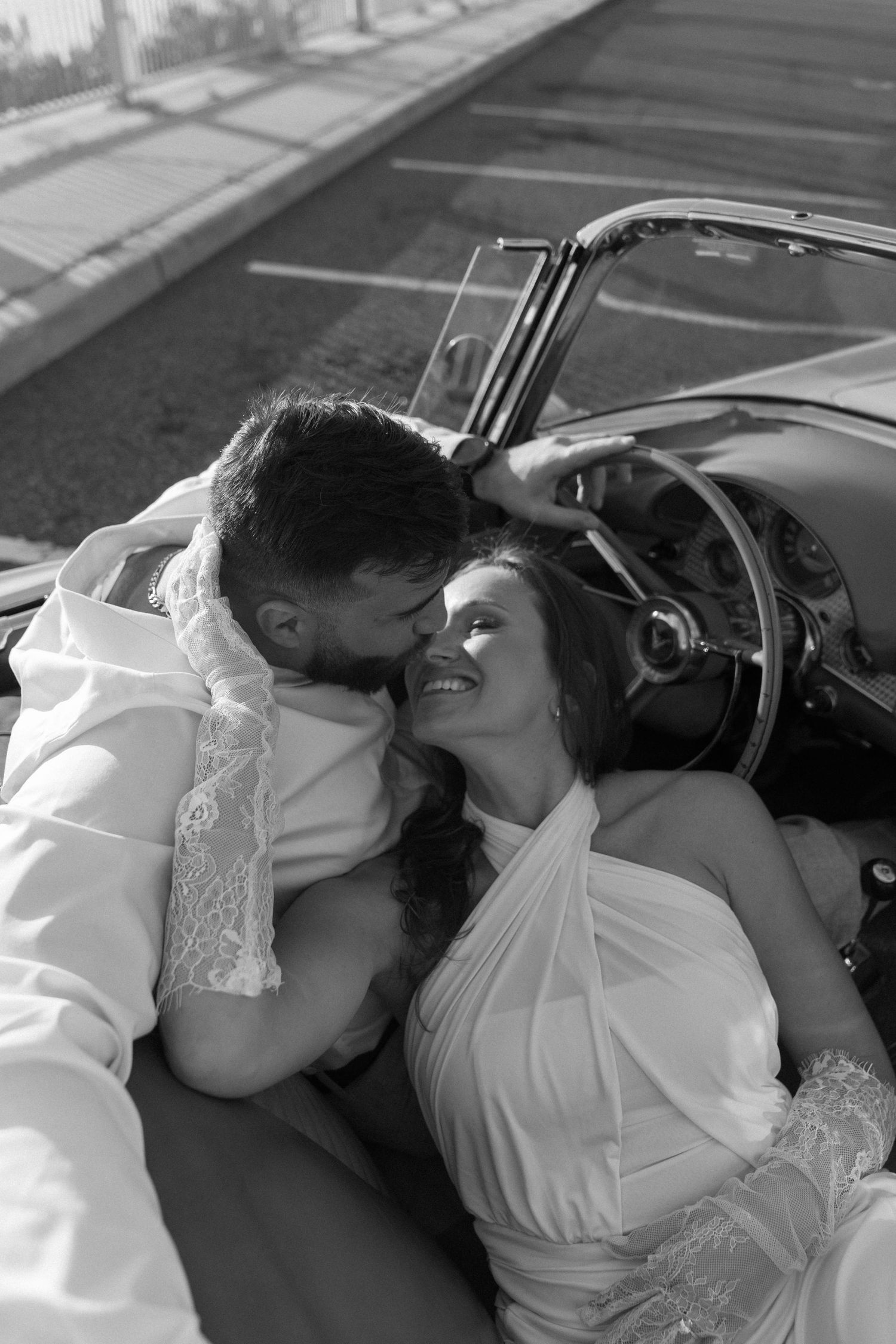 Black and white photo of a bride and groom sharing a romantic moment in a vintage convertible car.