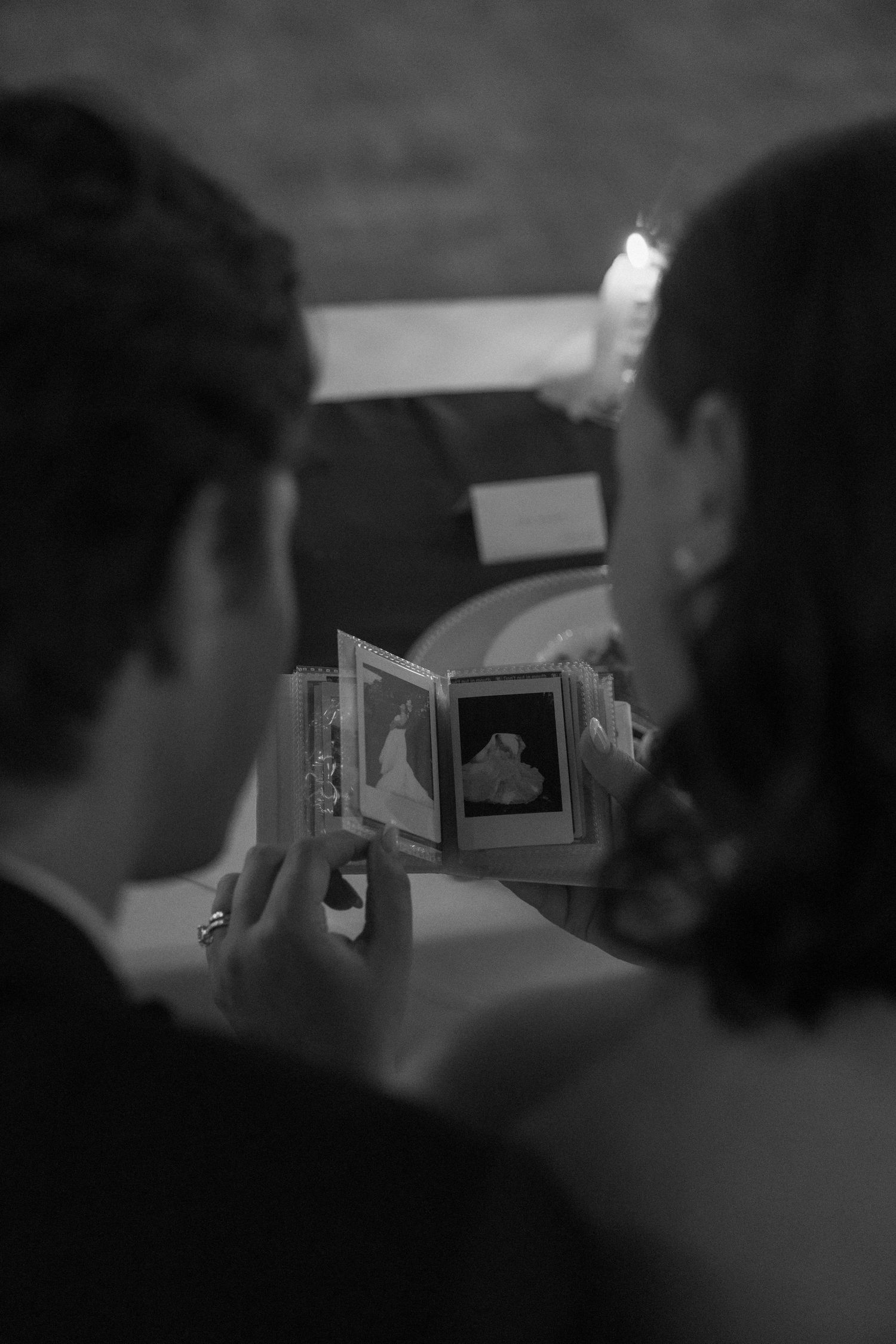 Couple viewing wedding photos in a small album together, black and white candid moment.