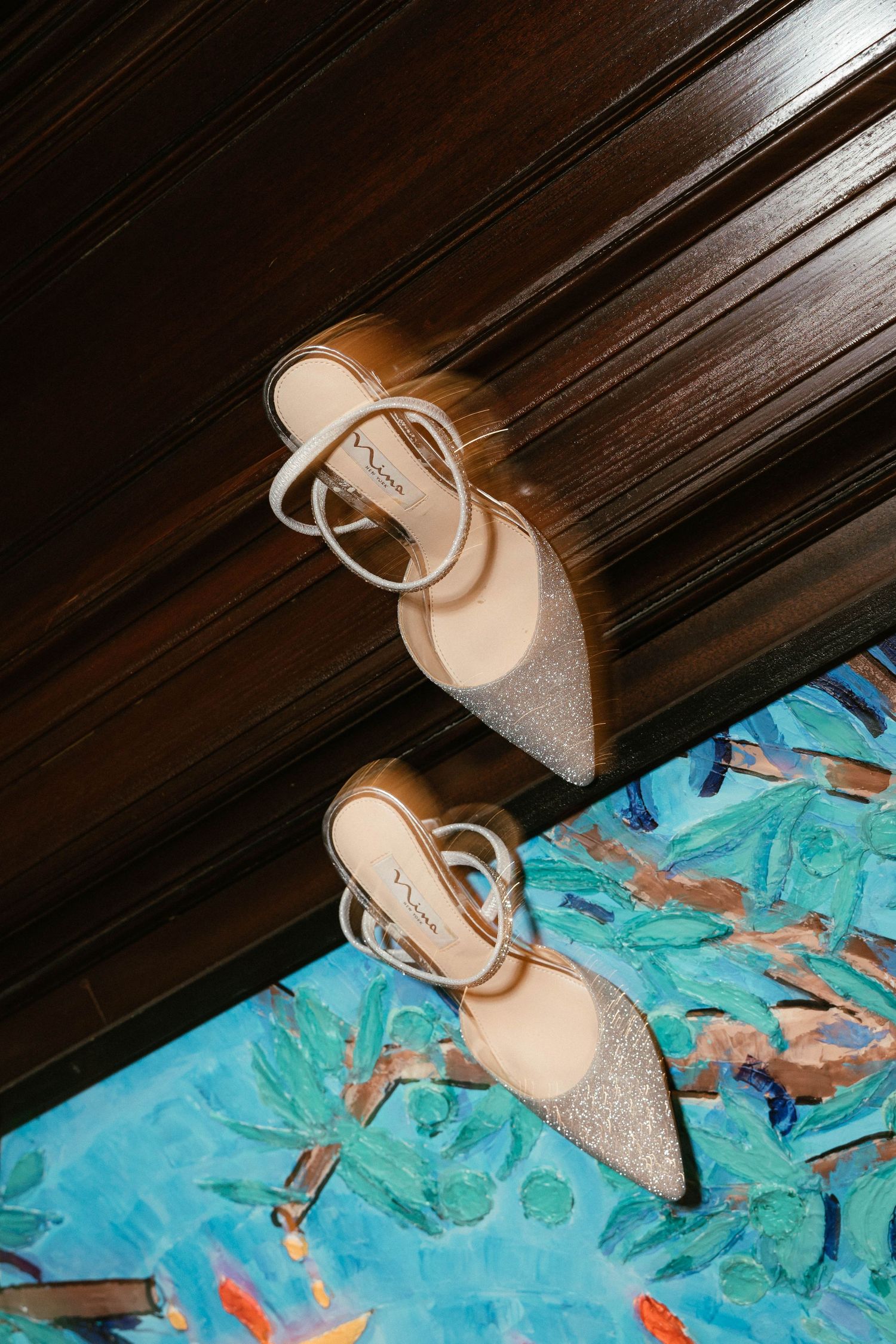 Sparkling silver bridal heels with ankle straps displayed on colorful painted floor surface.