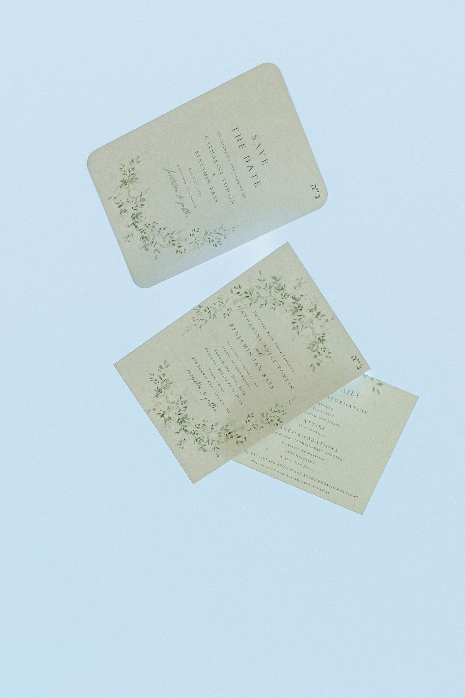 Elegant floral wedding invitations floating against soft blue background with greenery wreath design.
