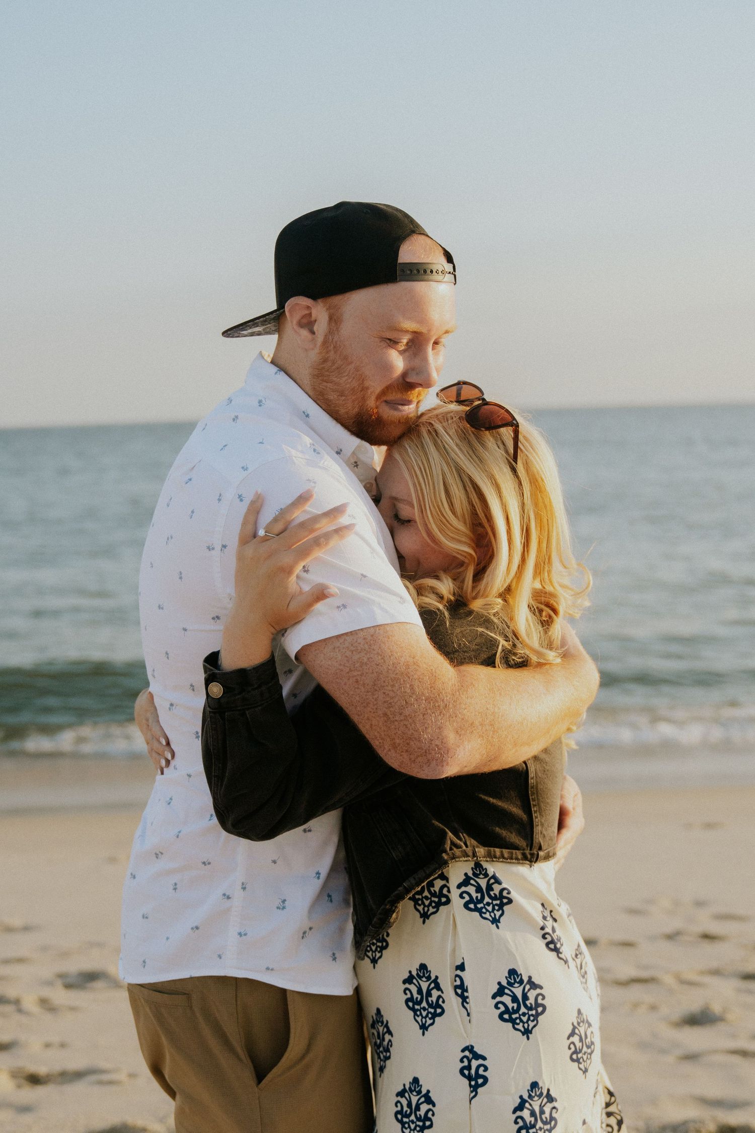 Couple embracing on a sandy beach at sunset near the ocean.