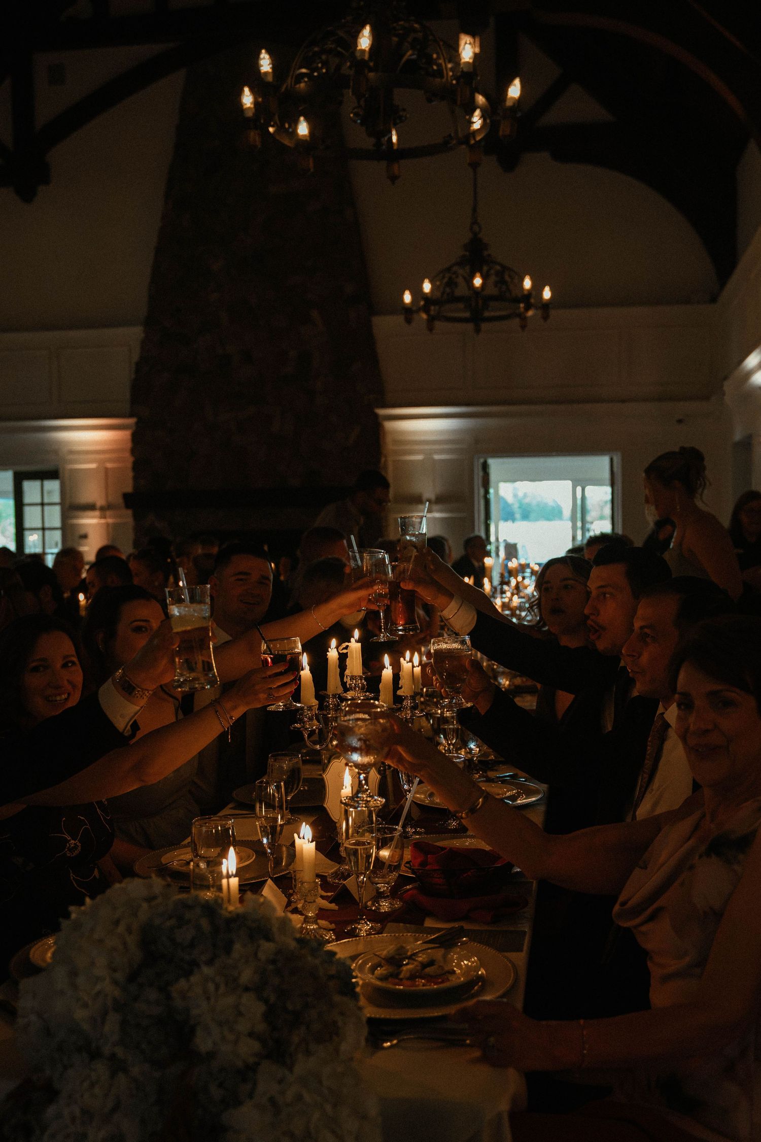 Wedding guests raising glasses in candlelit toast at elegant rustic reception dinner.