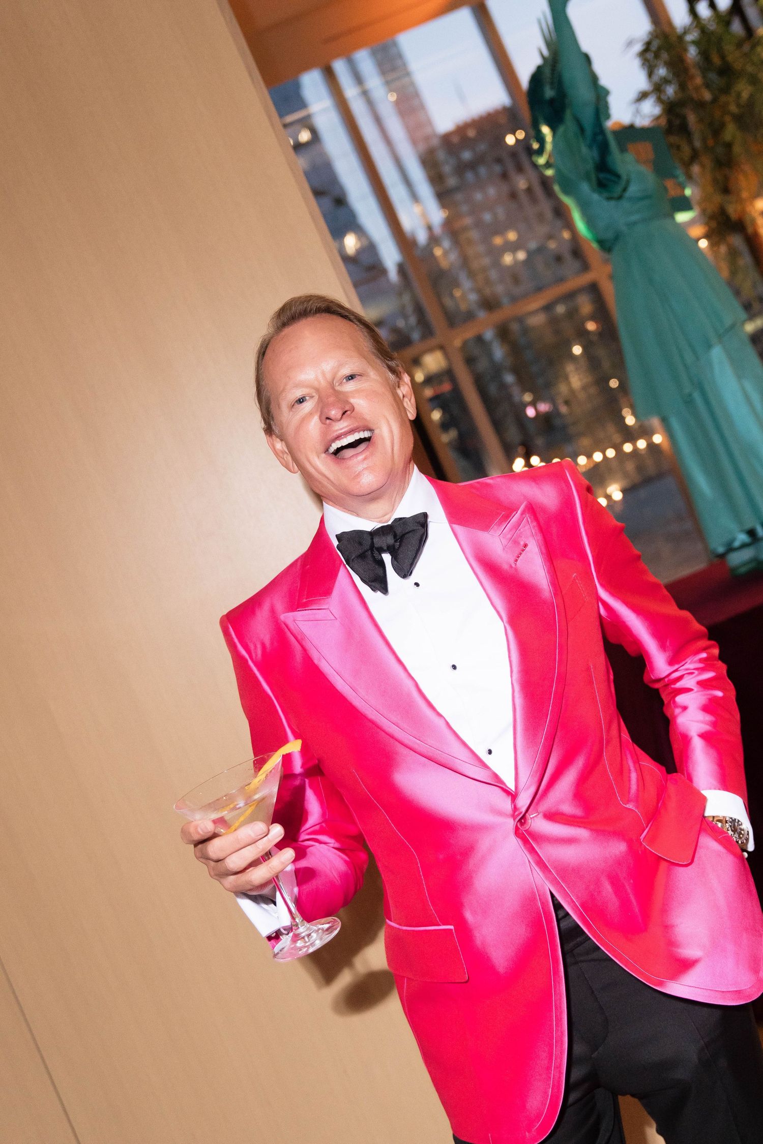 Cheerful man in bright pink satin tuxedo jacket holding a martini glass at a formal event.